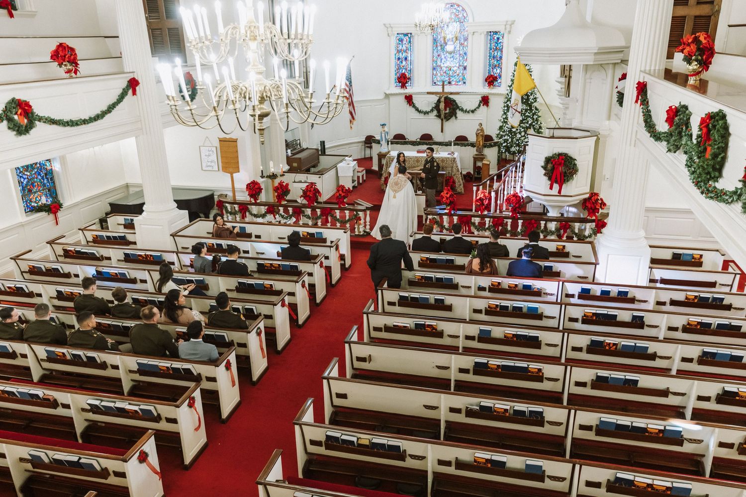 Aerial view of wedding ceremony in white church decorated with Christmas wreaths and red poinsettias.