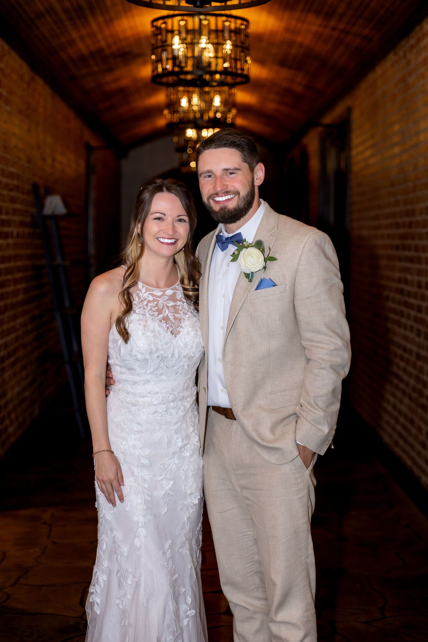 Smiling bride and groom posing together in a warmly lit brick corridor on their wedding day.
