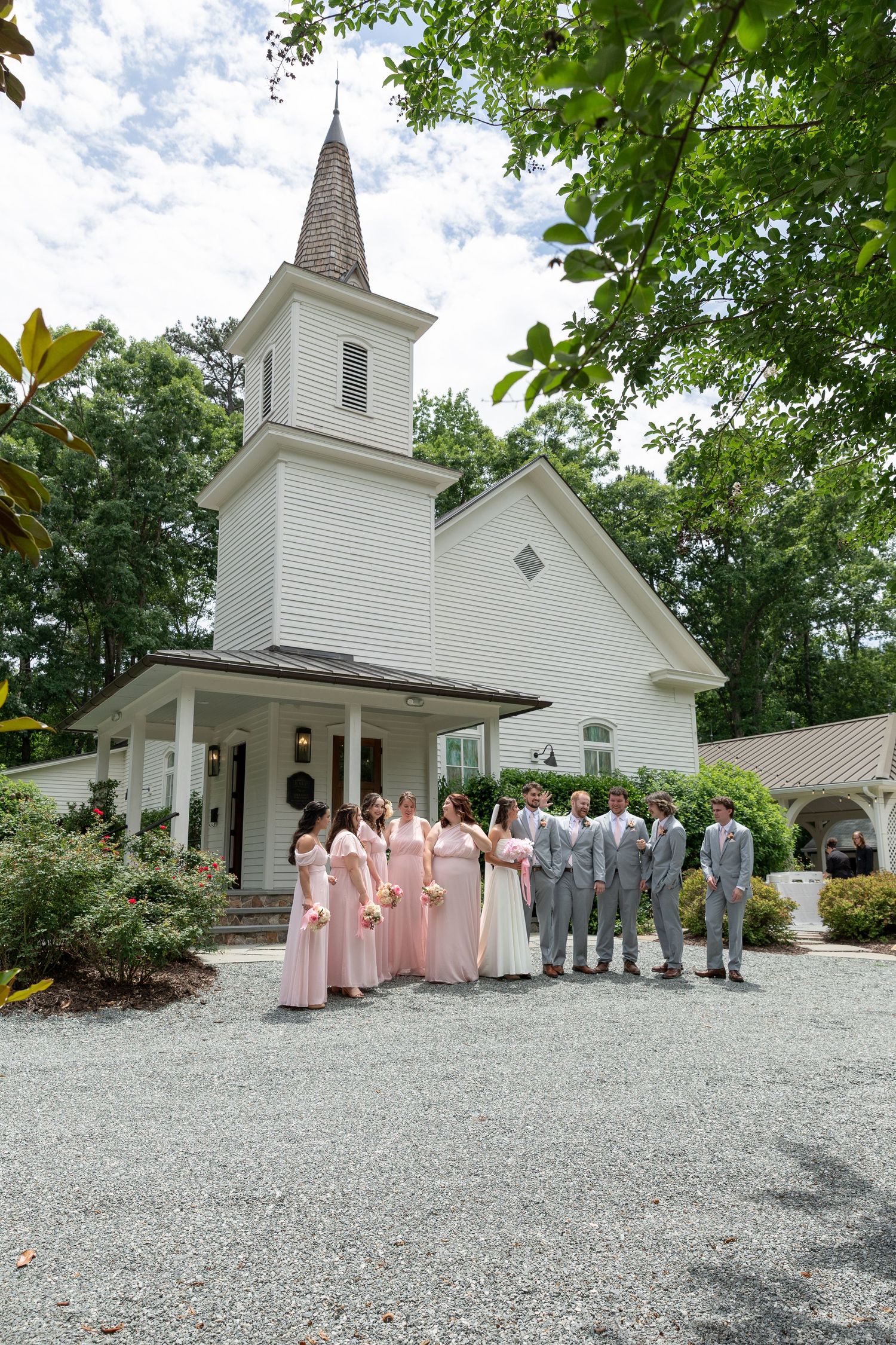 Wedding party posing in front of white chapel with bridesmaids in blush pink gowns.