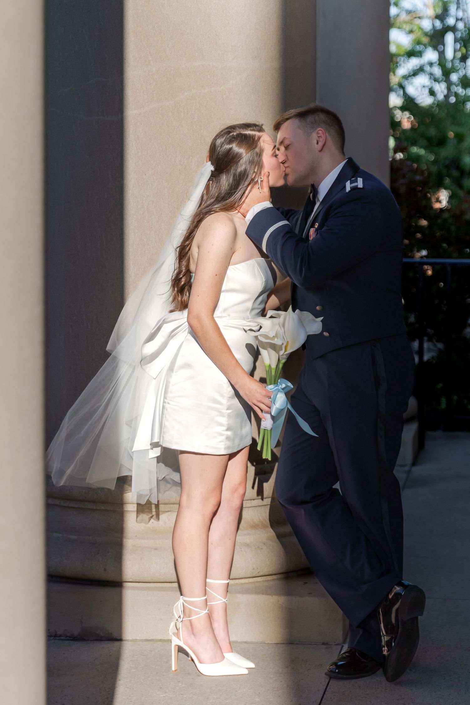 Bride and groom in Air Force uniform sharing a kiss leaning against a column after their courthouse wedding.
