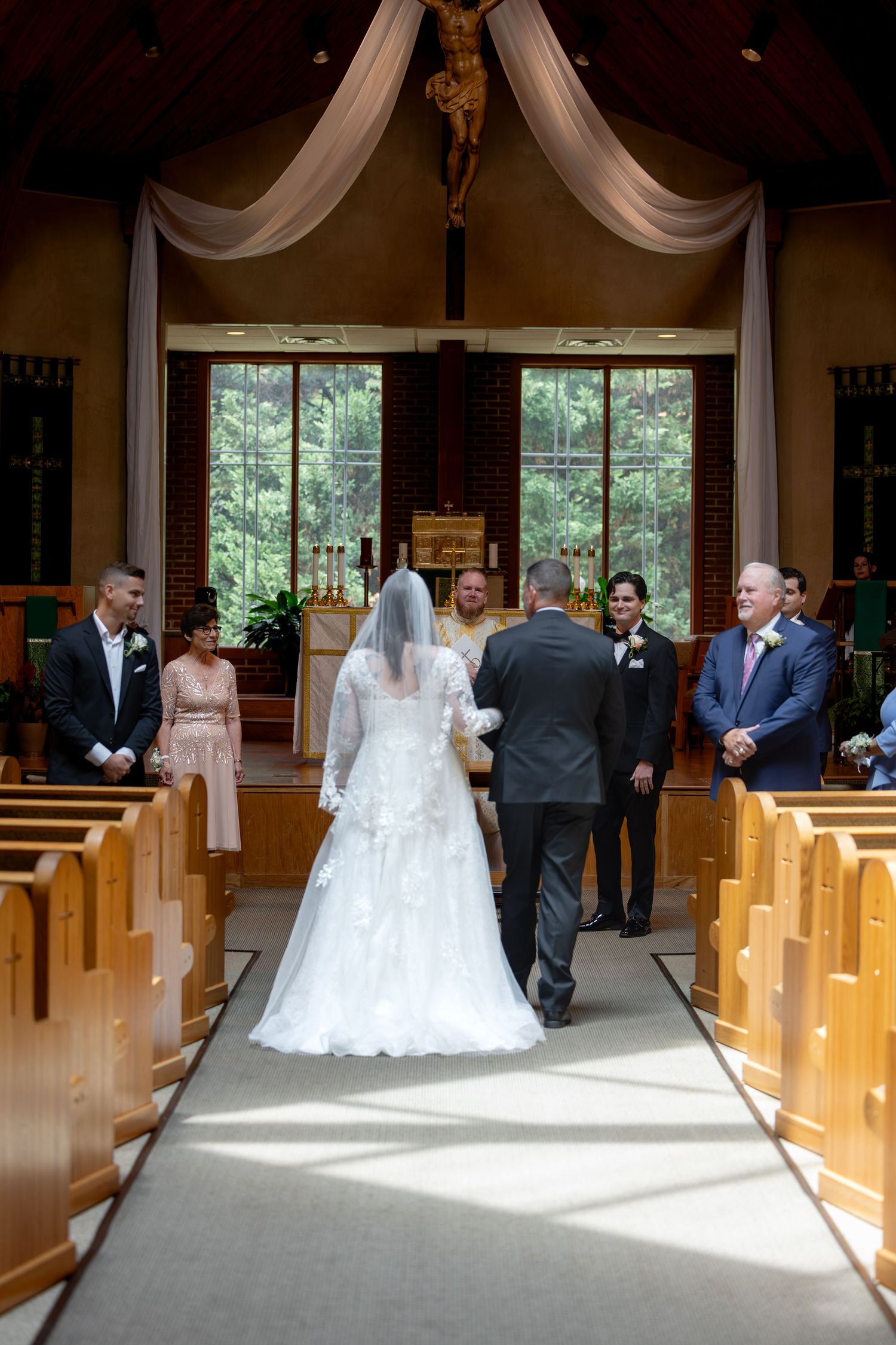 Bride walks down church aisle with escort during wedding ceremony, guests seated in wooden pews.