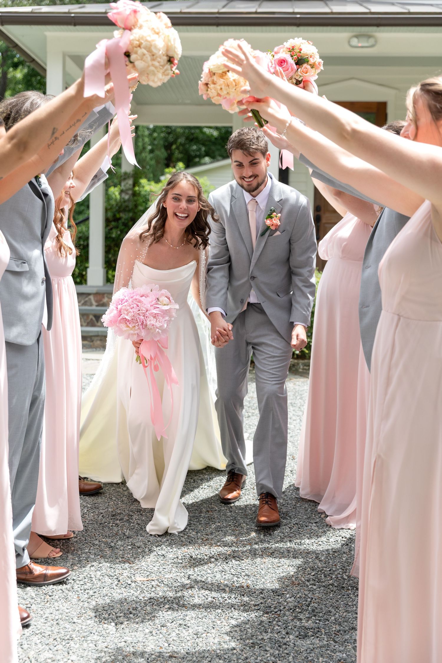 Joyful newlyweds walk through bouquet arch raised by bridesmaids and groomsmen after ceremony.