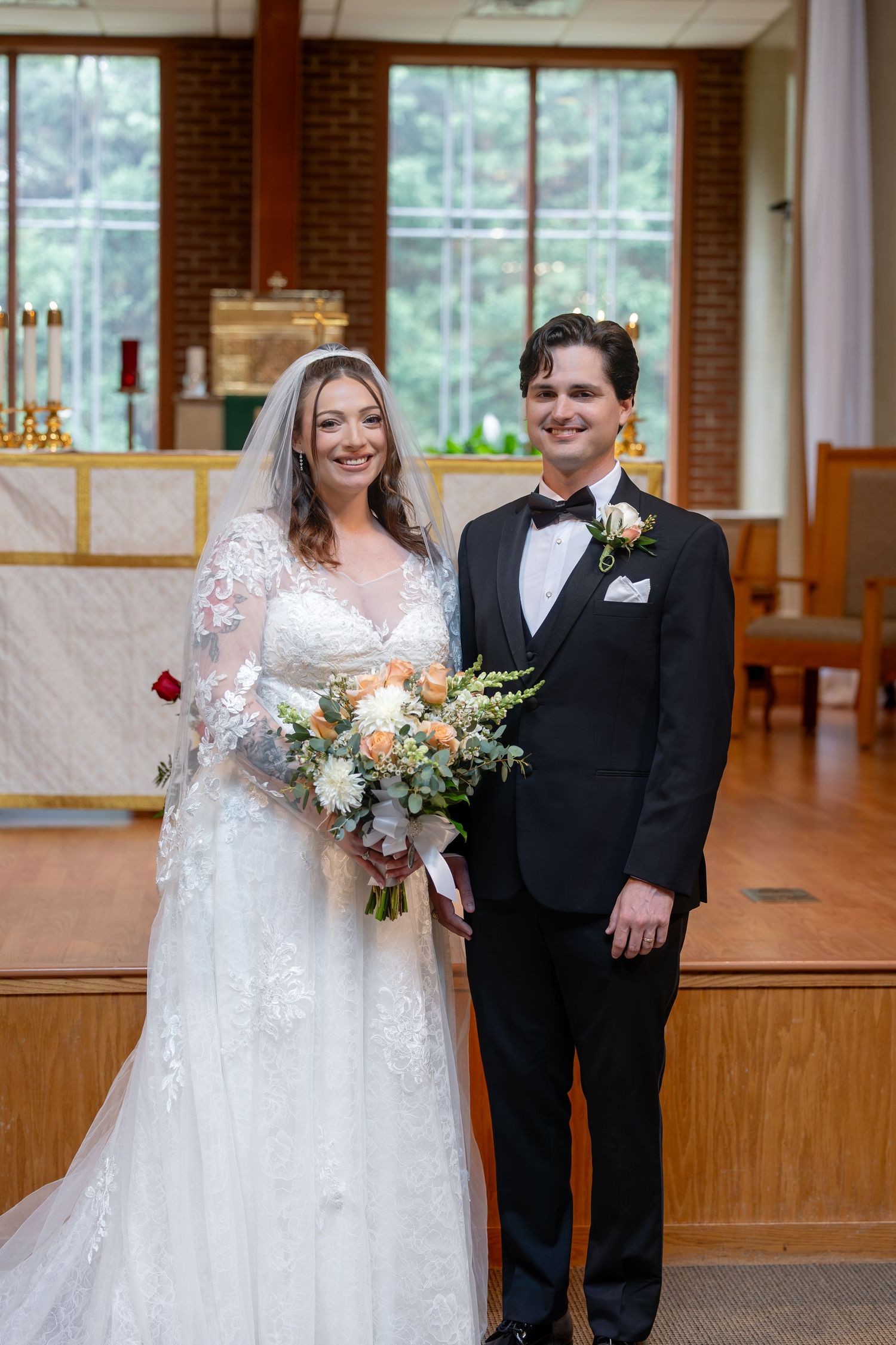 Bride and groom smiling together at church altar after wedding ceremony with bouquet.