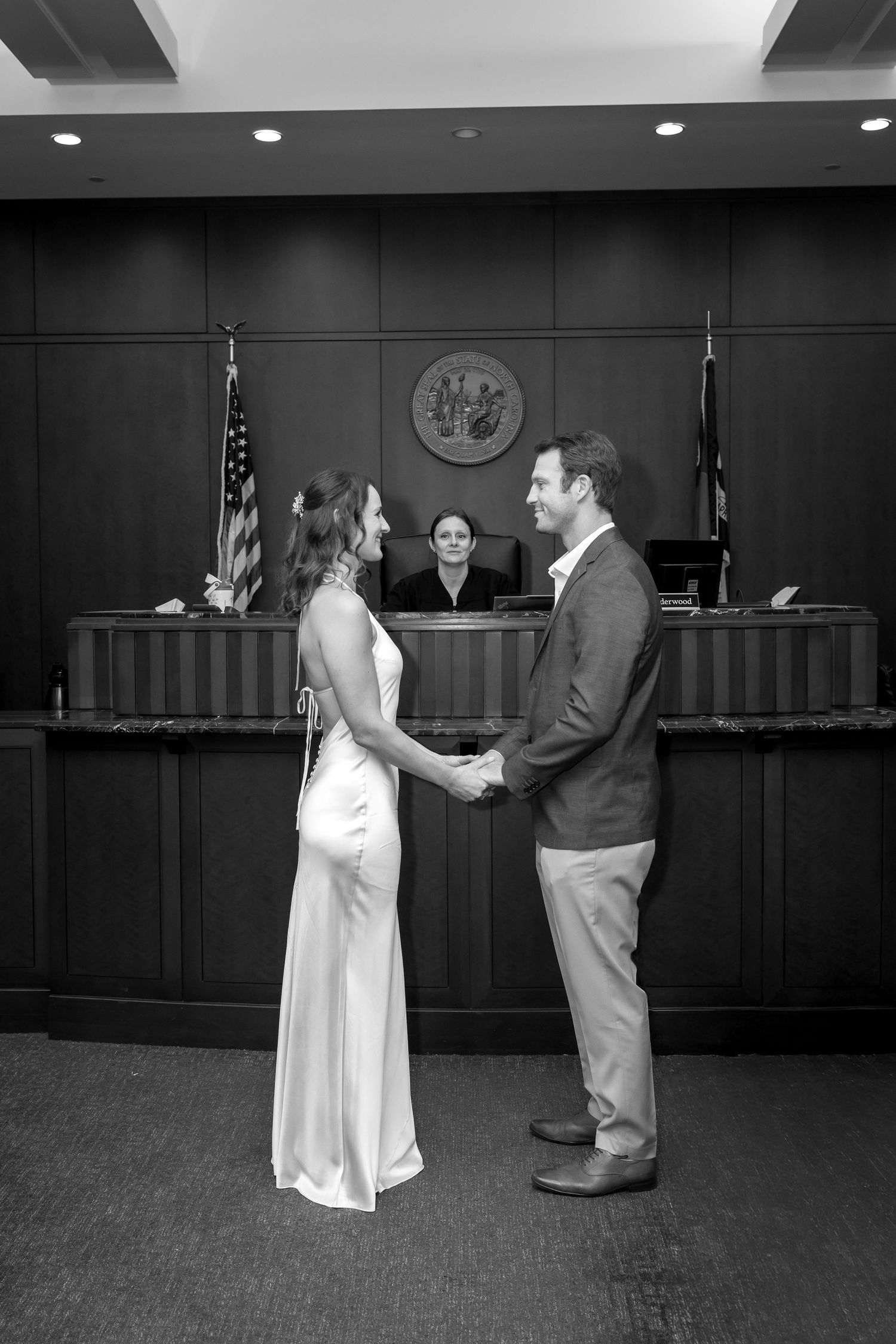 Black and white photo of a couple holding hands during a courthouse wedding ceremony with a judge presiding.