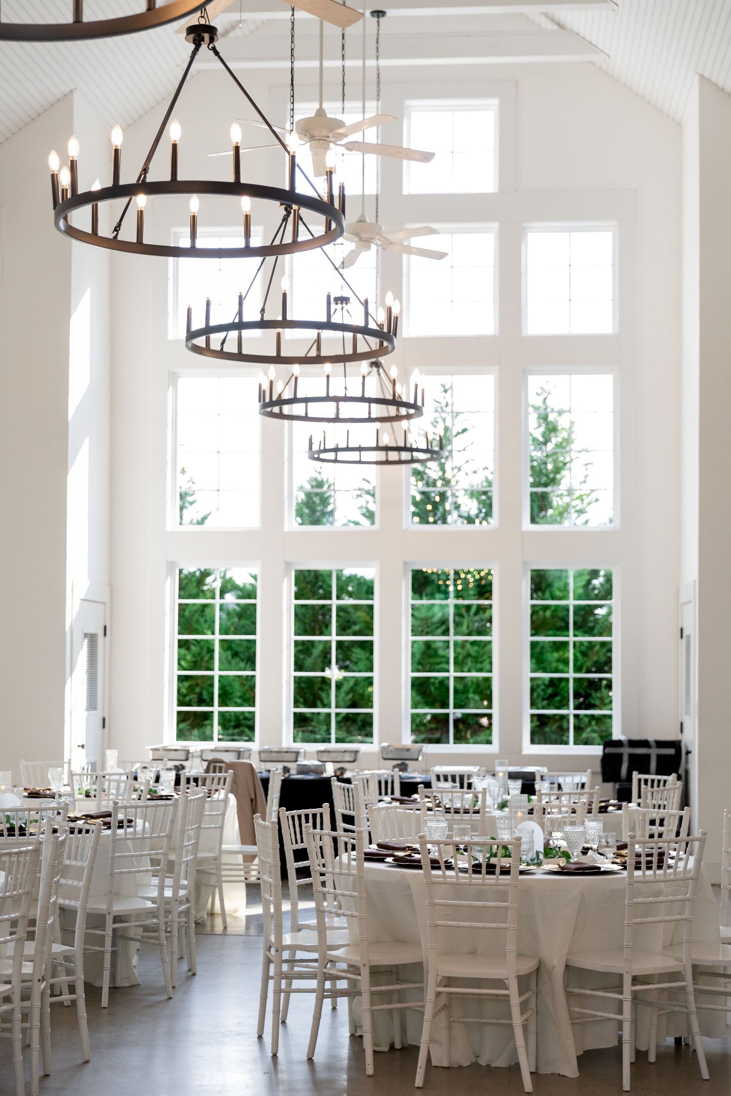 Elegant white wedding reception hall with wrought iron chandeliers and tall arched windows.