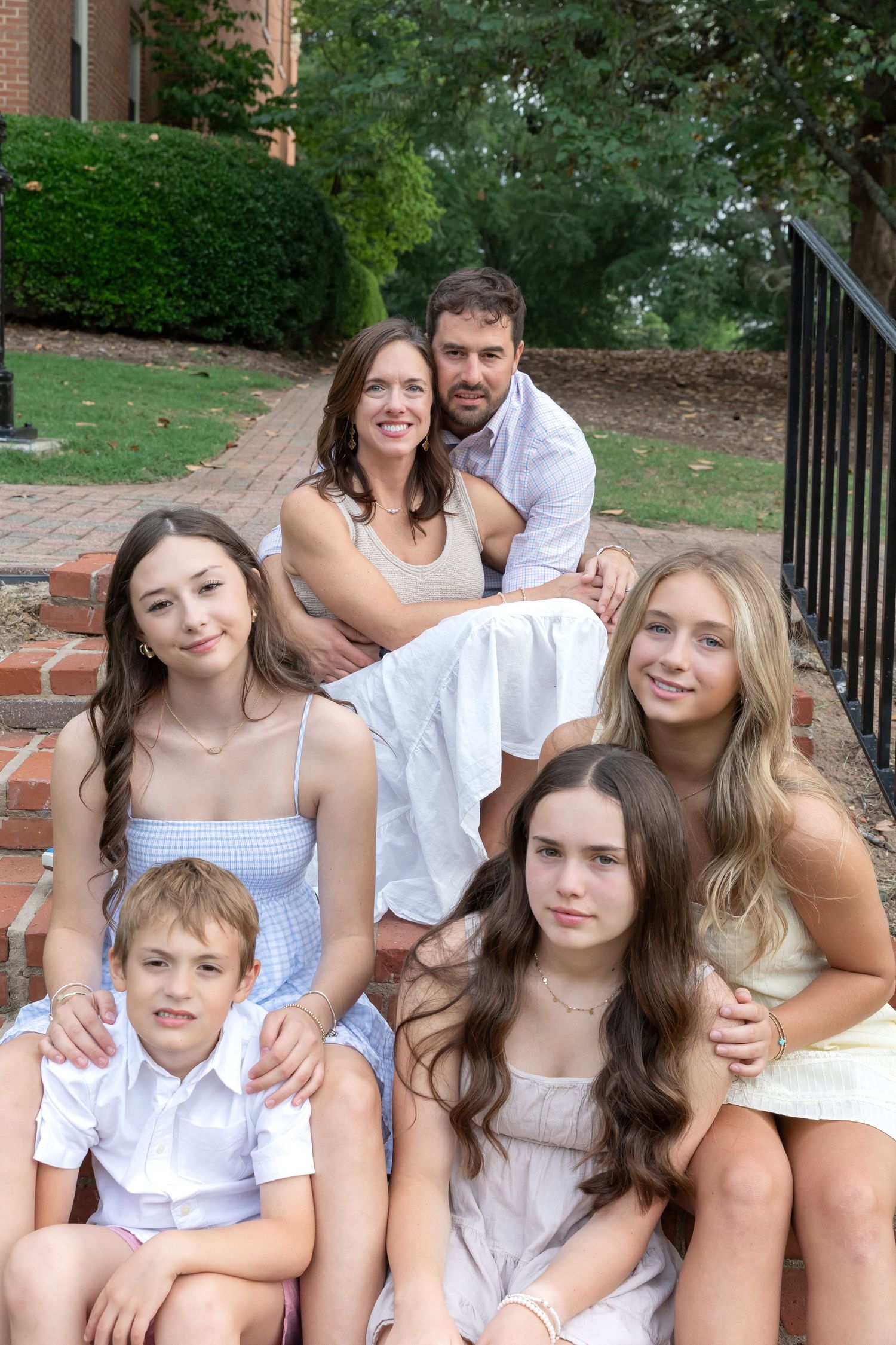 Family of six with parents and four children posing on brick steps outside a classic building.