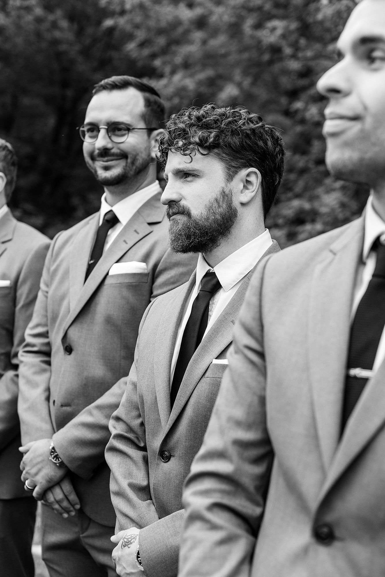 Groomsmen in matching gray suits stand together smiling during a wedding ceremony.