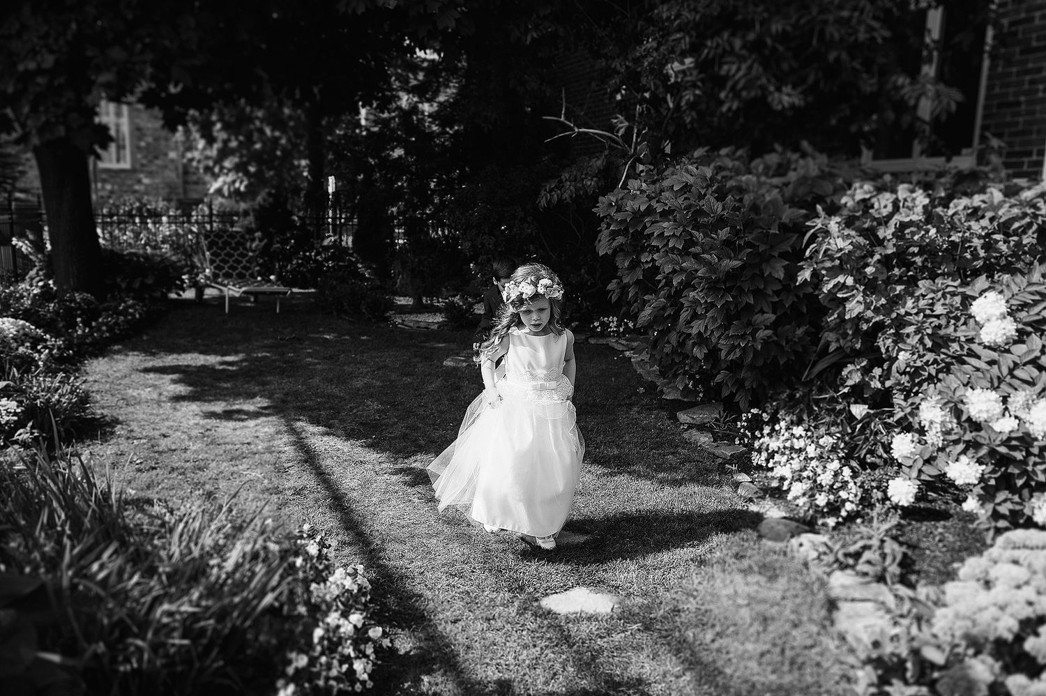 A black and white wedding dress floats ethereally along a winding garden path surrounded by lush foliage.