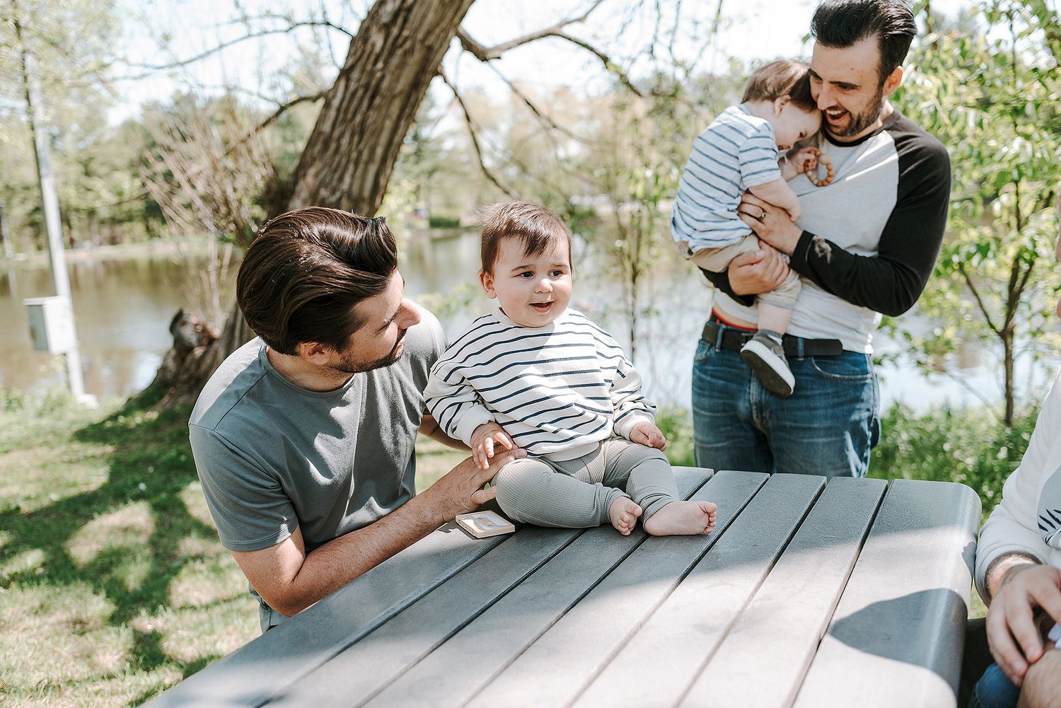 Series of casual outdoor family photos taken at a wooden picnic table by the water.