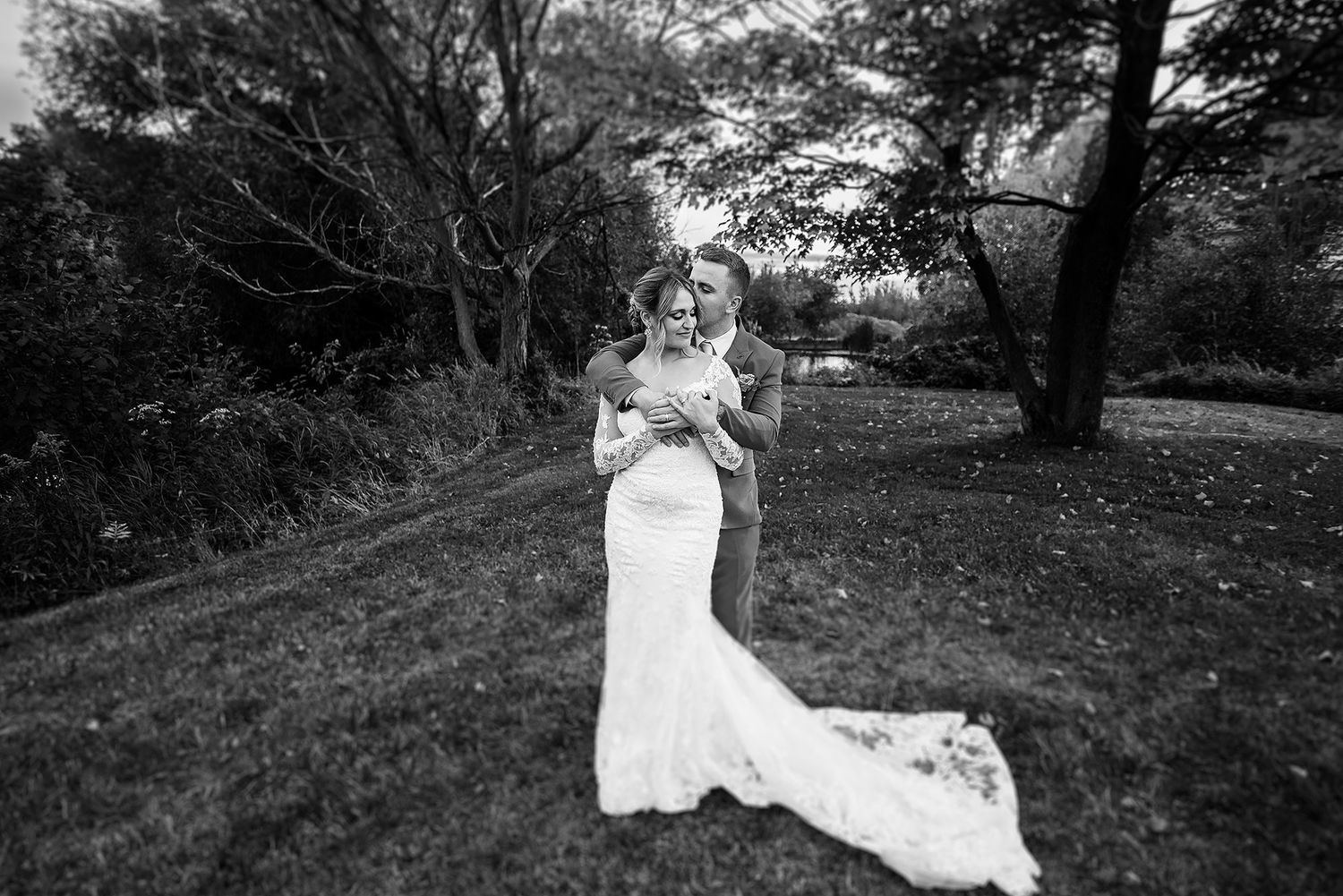 A couple embraces in a romantic outdoor wedding photo with a flowing white dress against a natural wooded backdrop.