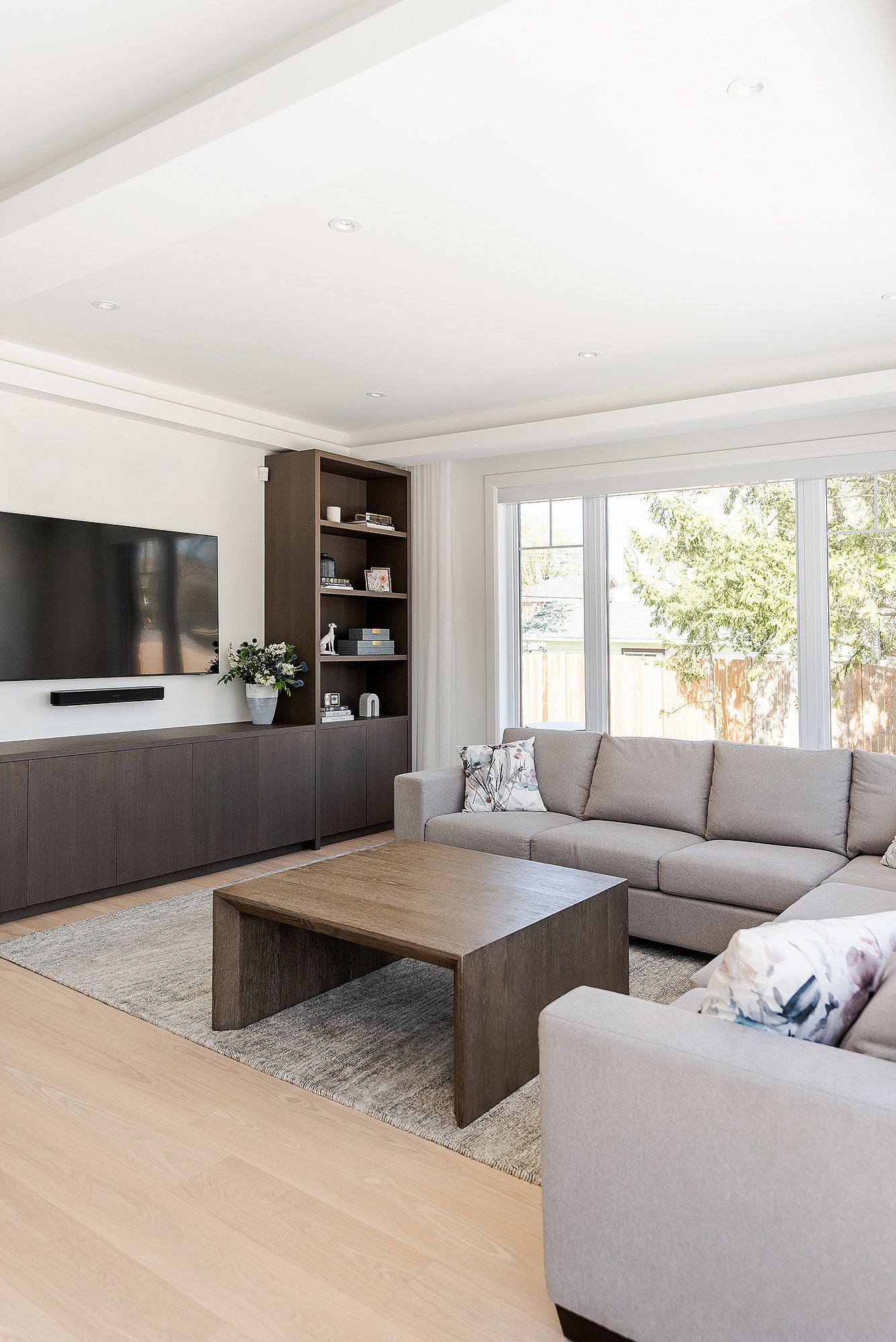 Modern living room interior with gray sectional sofa, dark wood built-ins, and light hardwood flooring.