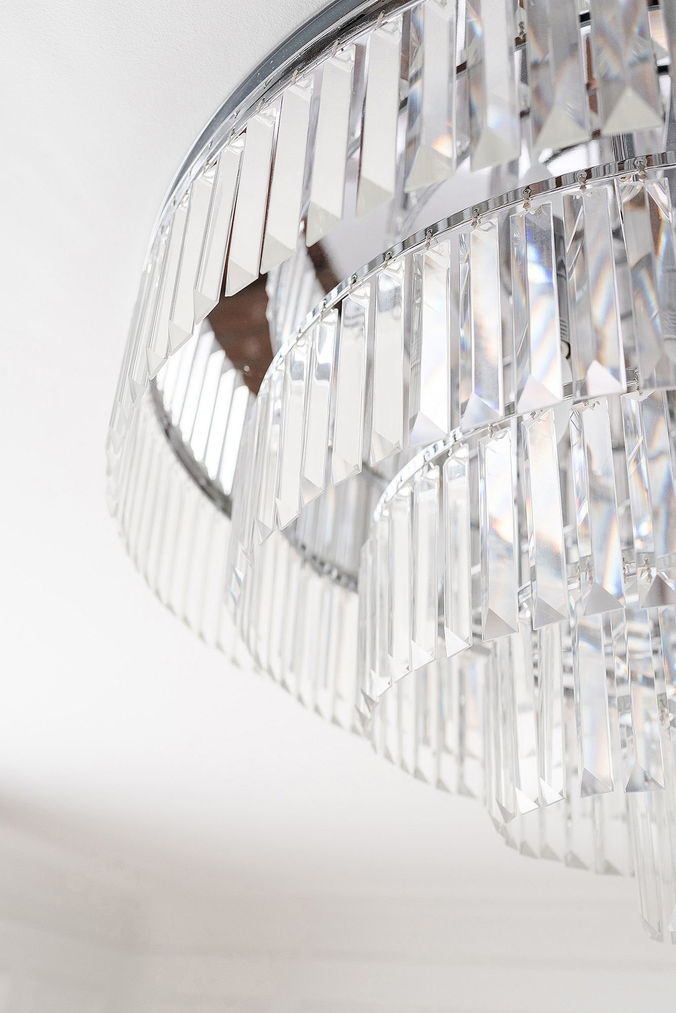 Crystal chandelier with prismatic glass elements creating a dramatic lighting effect against white background.