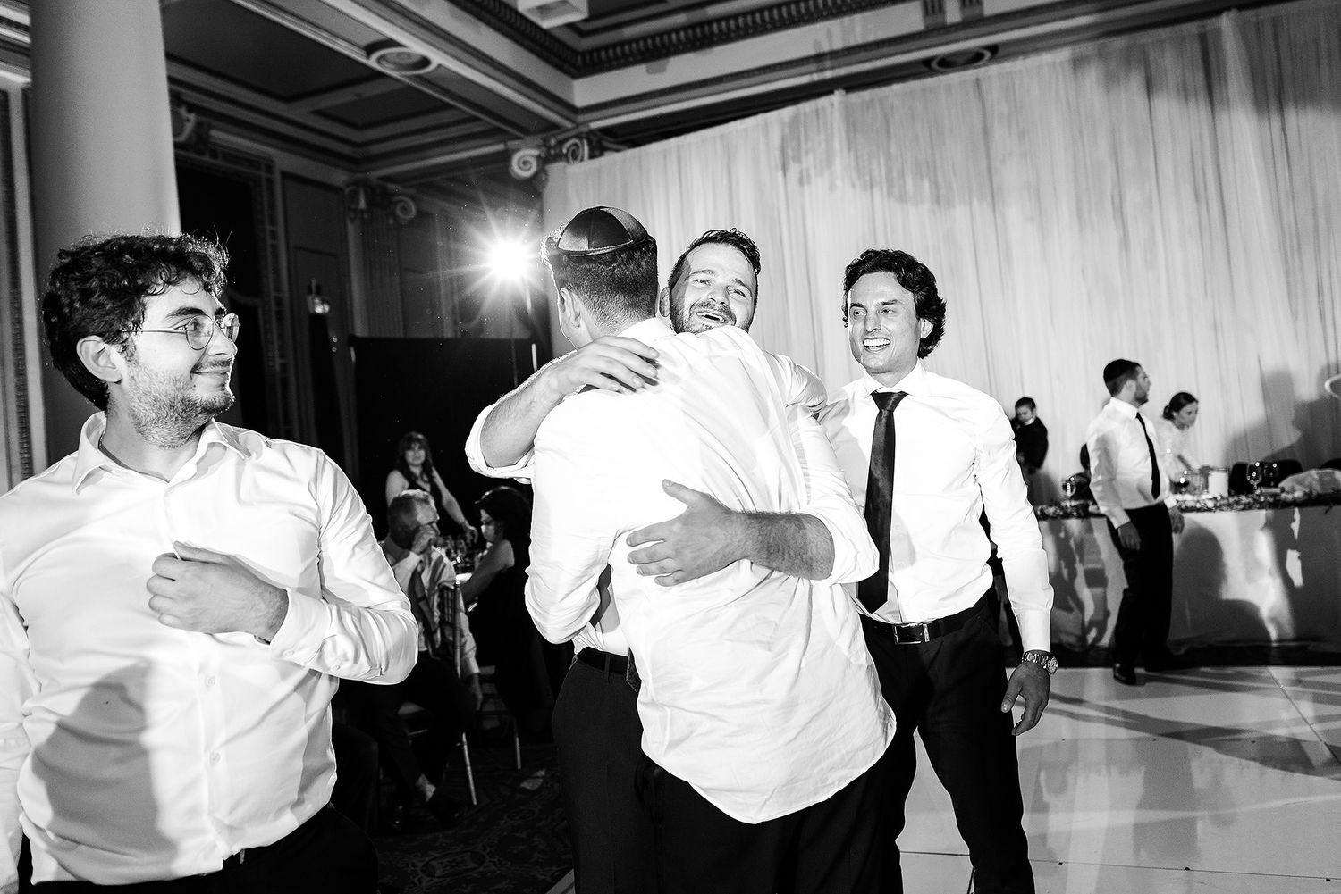Black and white photo of people dancing and embracing at an indoor celebration.