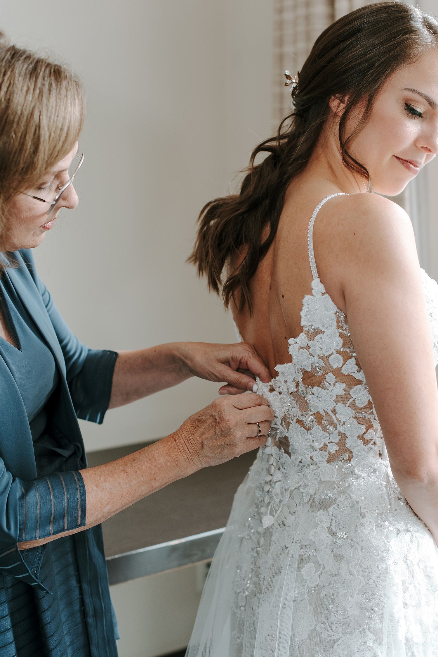A wedding dress being buttoned up showing delicate lace details and floral appliques along the back.