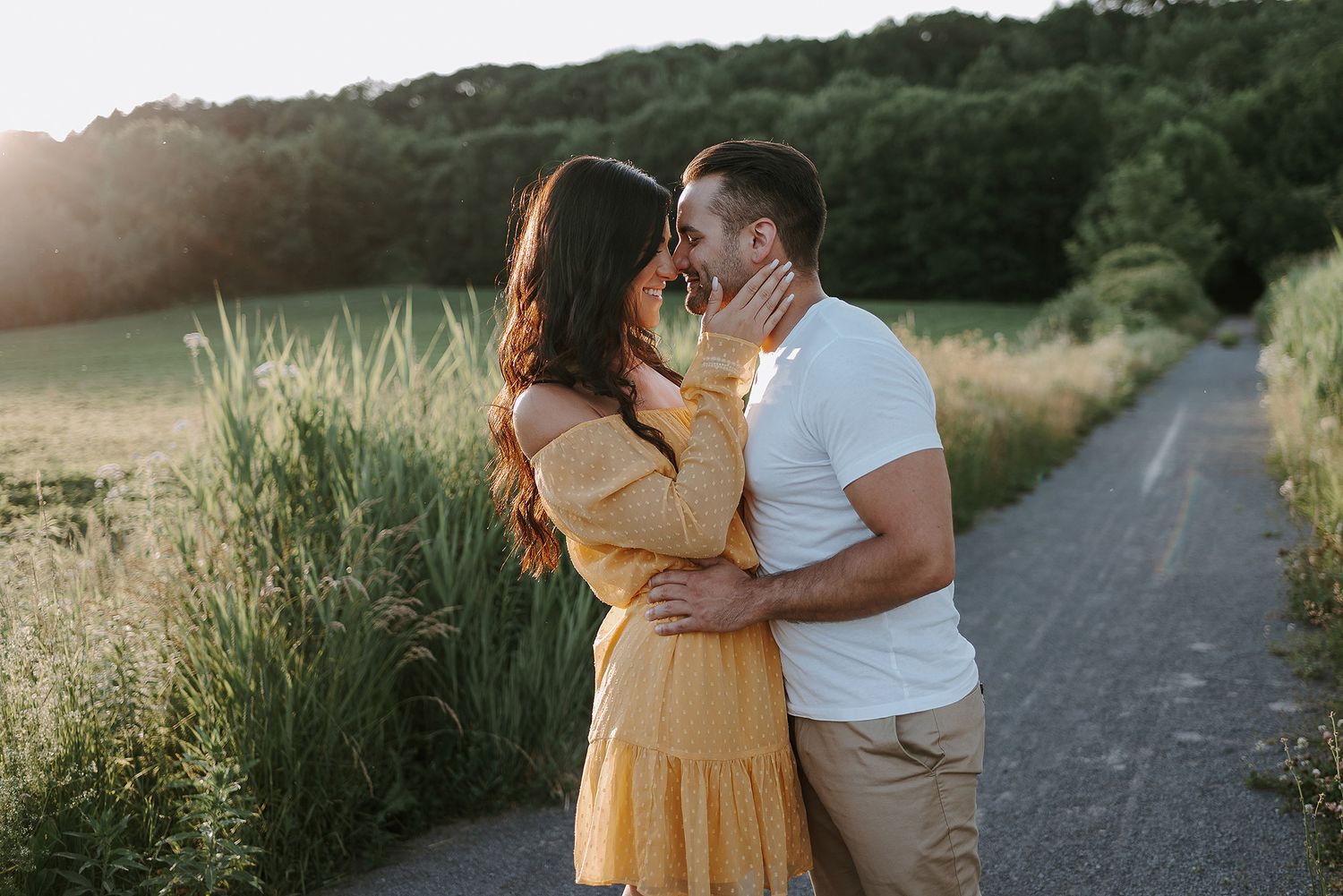 Romantic couple walking together on a dirt path surrounded by tall grass during golden hour.