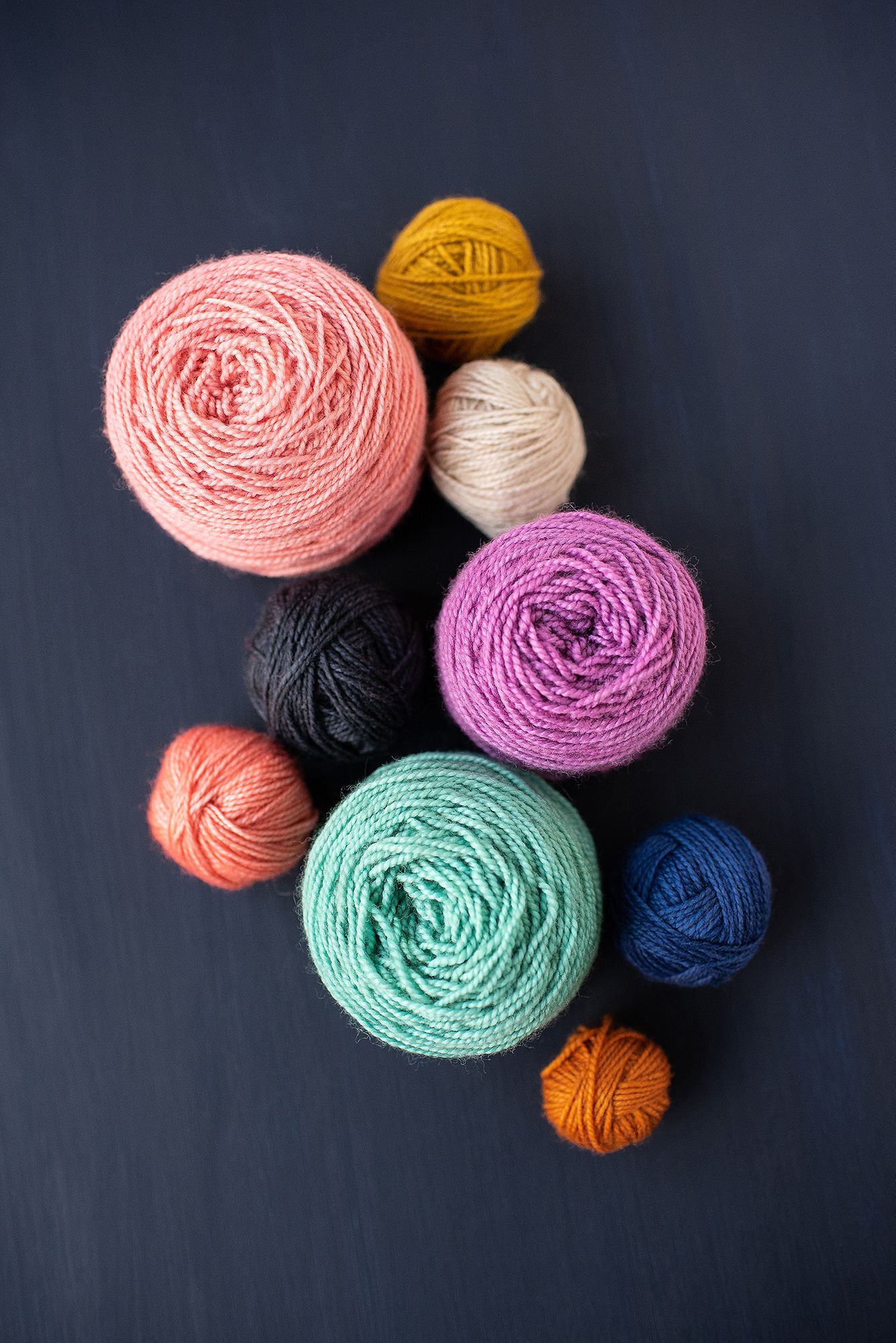 Assorted balls of yarn in pastel colors arranged on dark background.