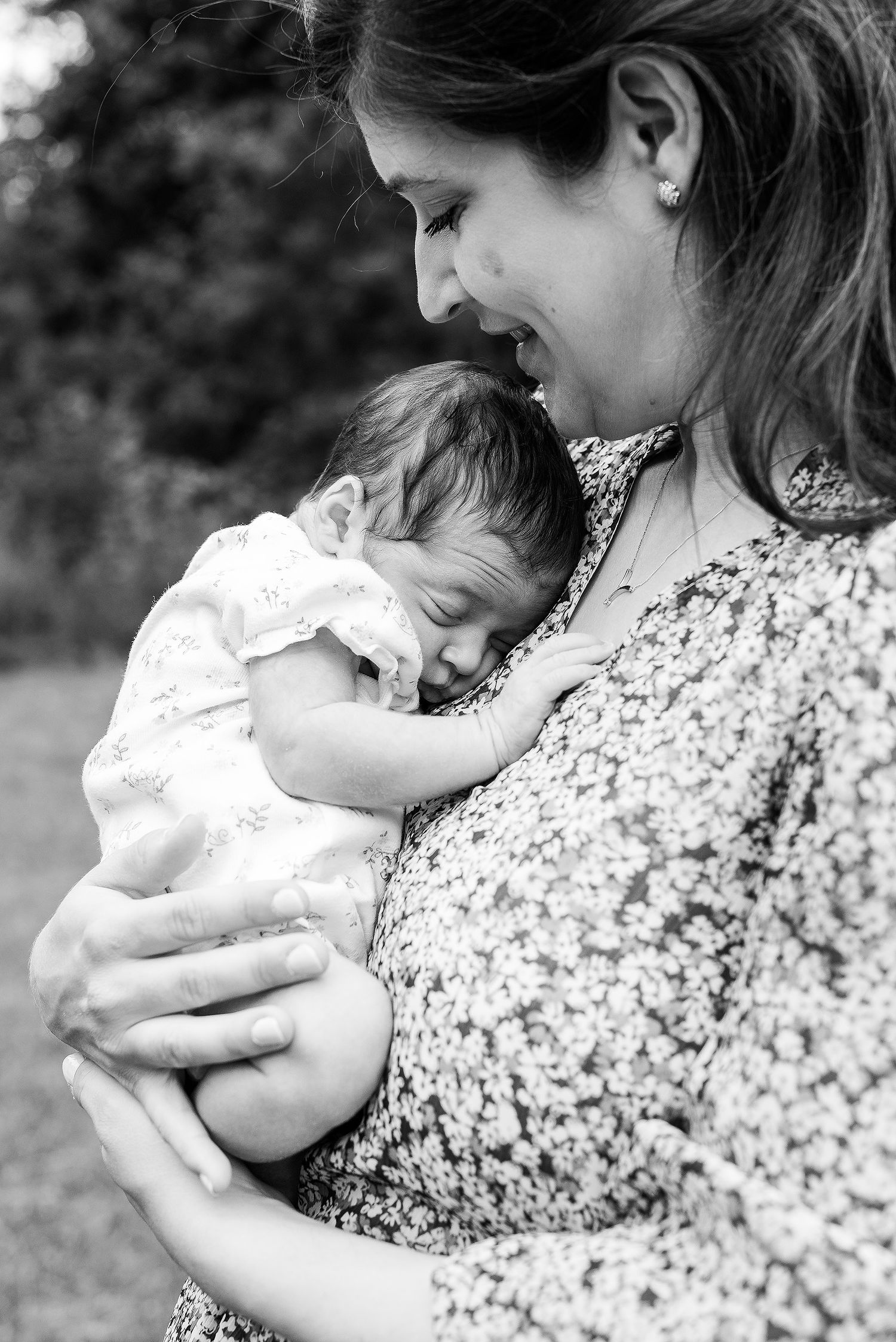 A black and white portrait of tender moment between parent and sleeping baby outdoors.