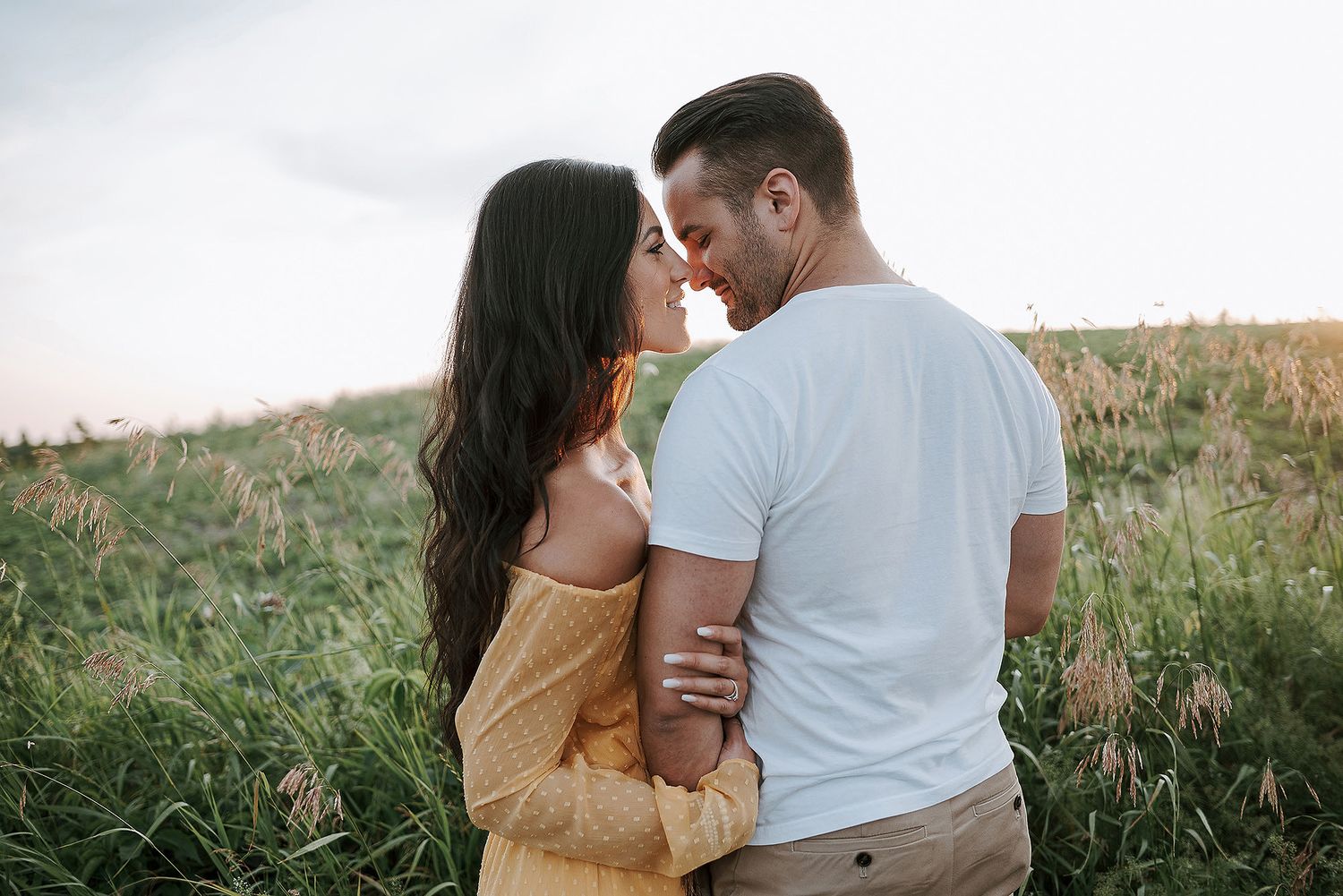 Romantic couple embraces in a golden field at sunset during a dreamy outdoor photo session.