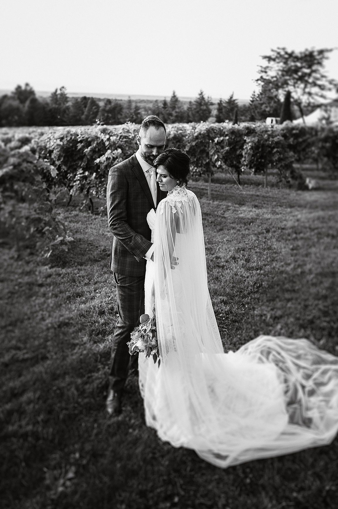 A black and white wedding photo series showing a couple with flowing veil in a countryside setting.
