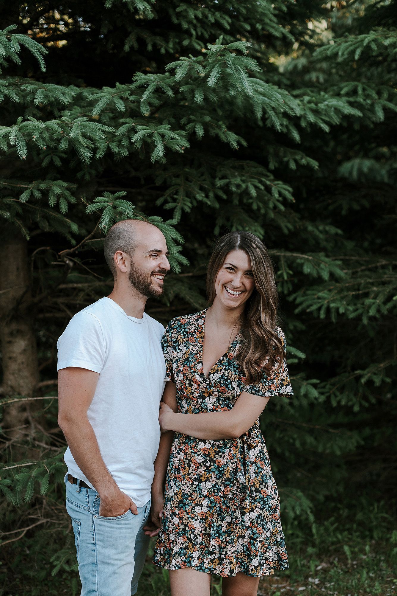 A joyful couple laughing together against a backdrop of evergreen trees.