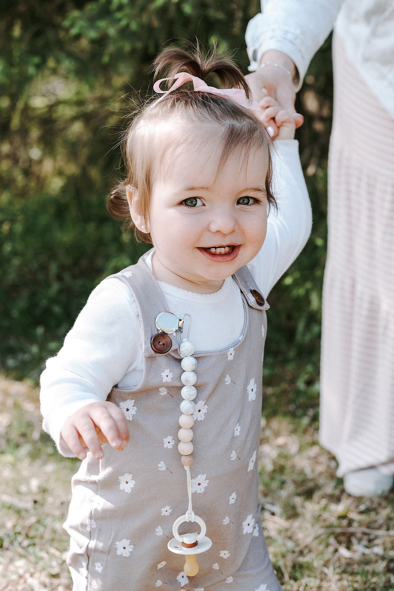 Child wearing floral patterned beige dress with white accents in outdoor garden setting.