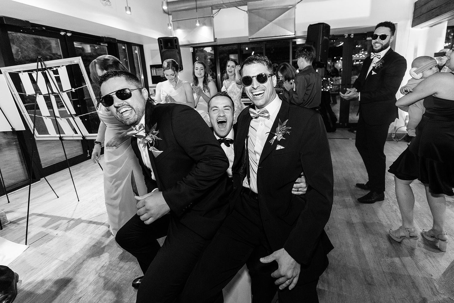 Wedding guests in formal attire dance and celebrate on the dance floor at a reception venue.