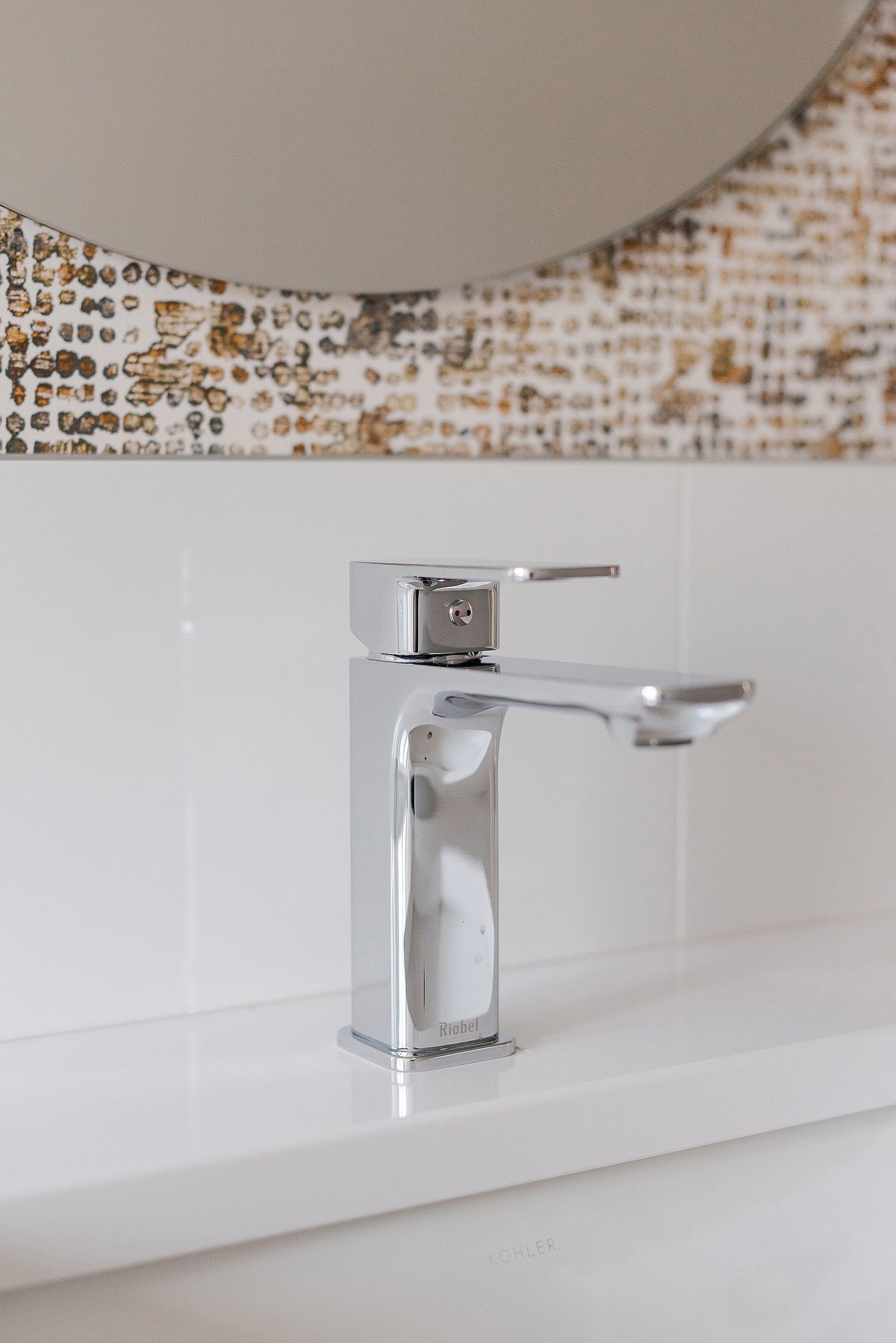 Modern chrome bathroom faucet on white counter against textured metallic wallpaper.