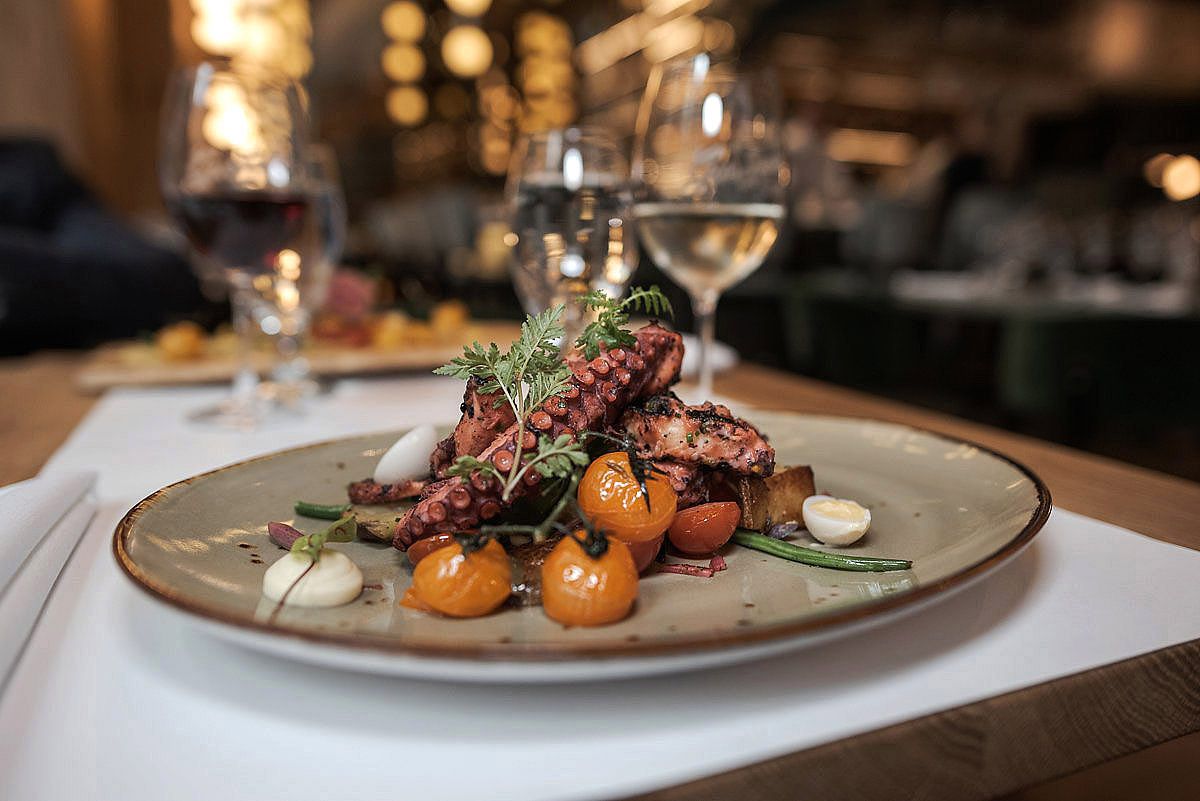 Elegant plated dishes in a dimly lit upscale restaurant setting with warm ambient lighting and modern presentation.