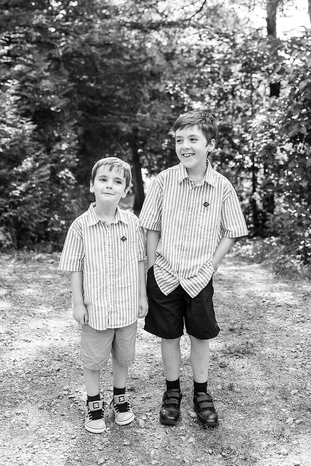 Two children in matching striped shirts and dark shorts stand together on a dirt path in a black and white photo.
