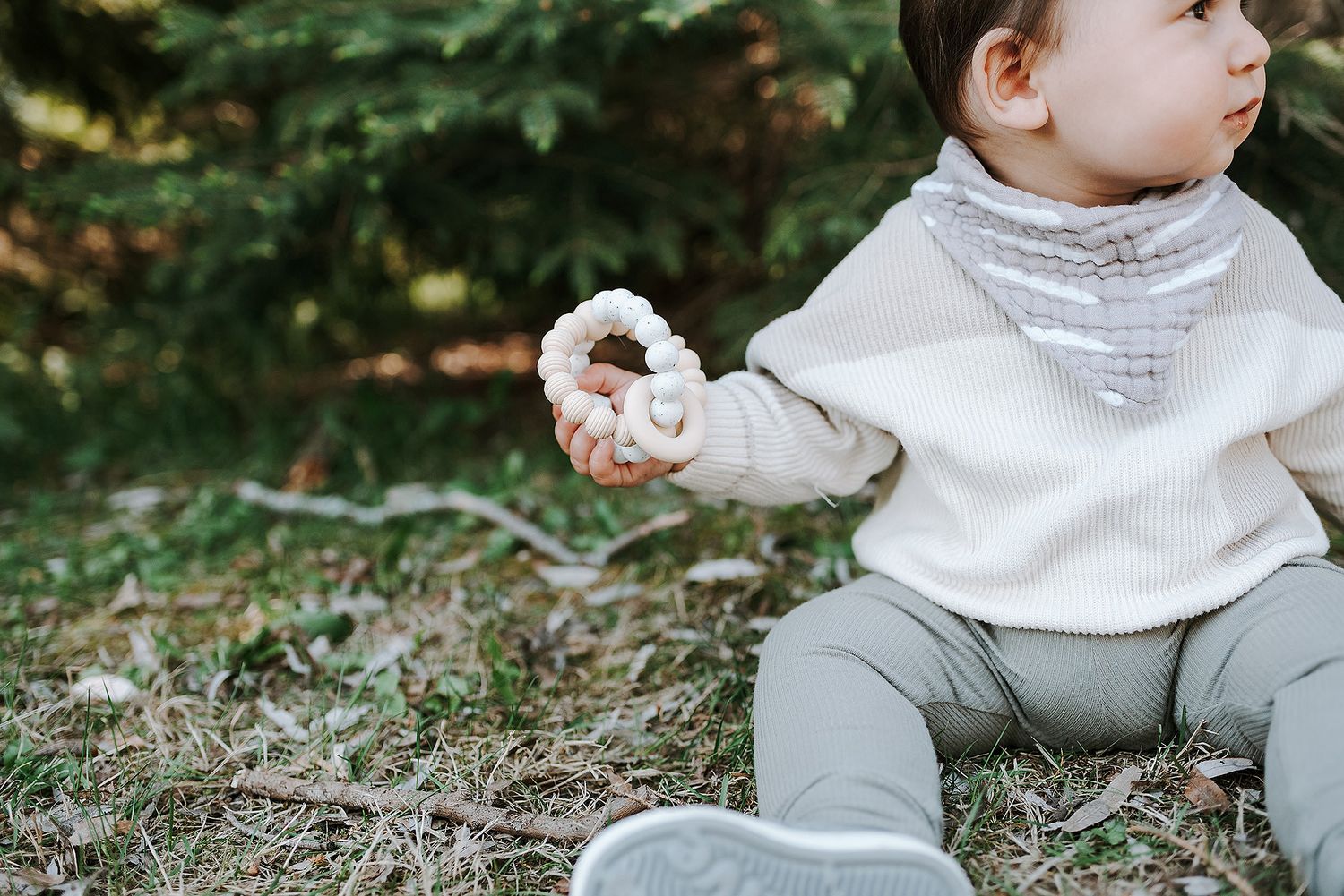 Baby in cozy white sweater sitting outdoors with a contemplative side profile.