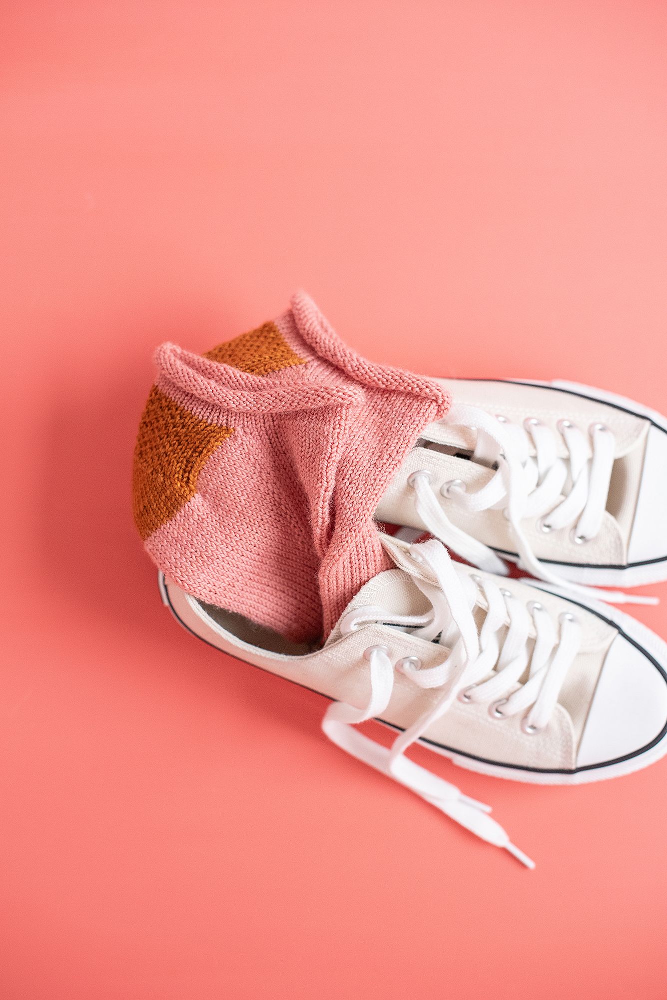 Pink knitted sock paired with white canvas sneaker on coral background.
