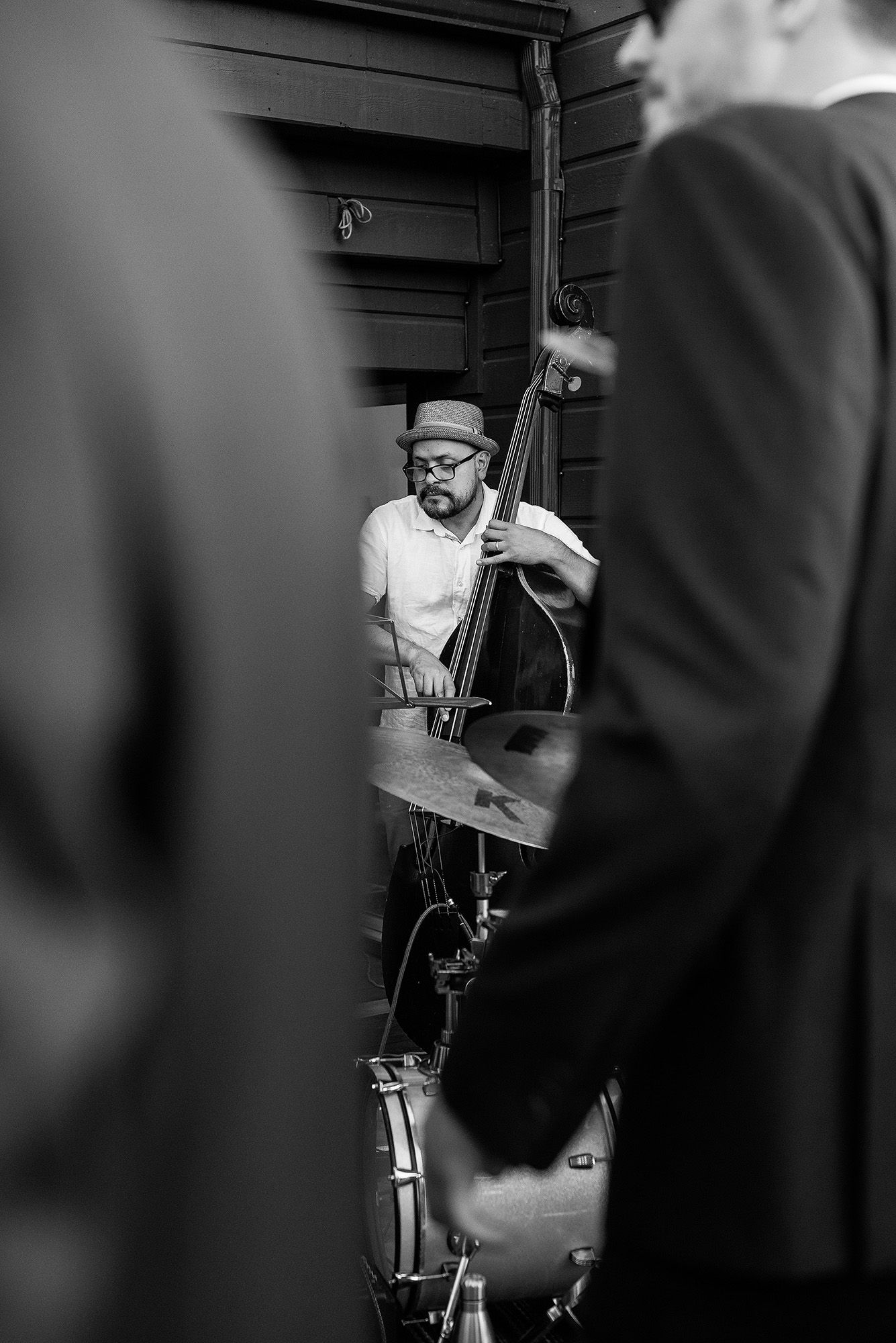 Black and white photo of a jazz drummer performing with brushes on a drum set in a dimly lit space.