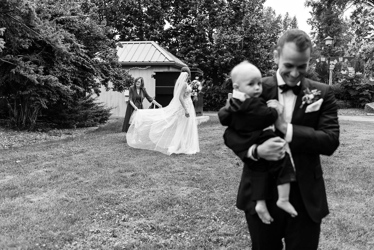 A series of black and white photos showing a baby being playfully tossed in the air outdoors.