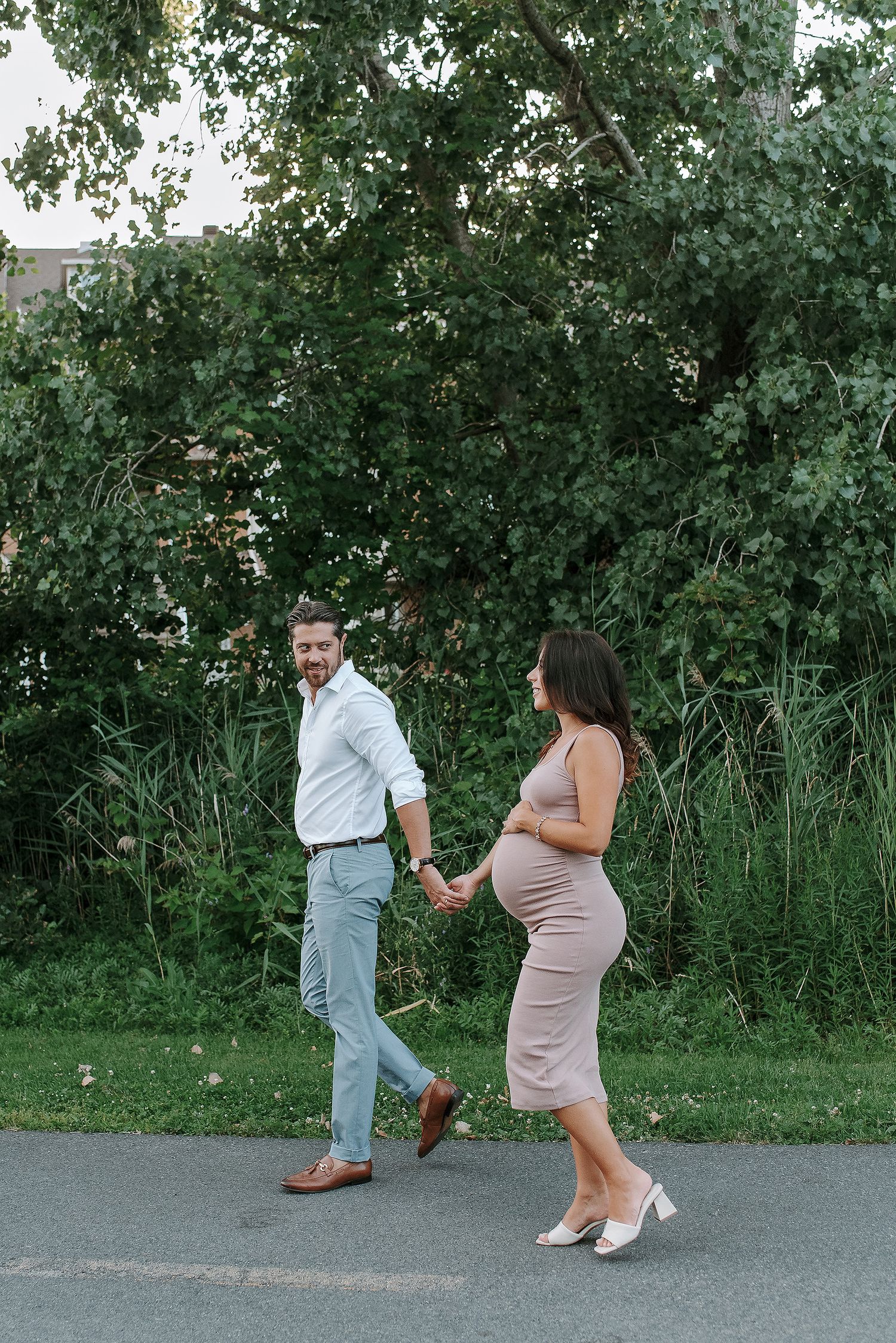 A couple dances playfully on a paved path surrounded by lush greenery.