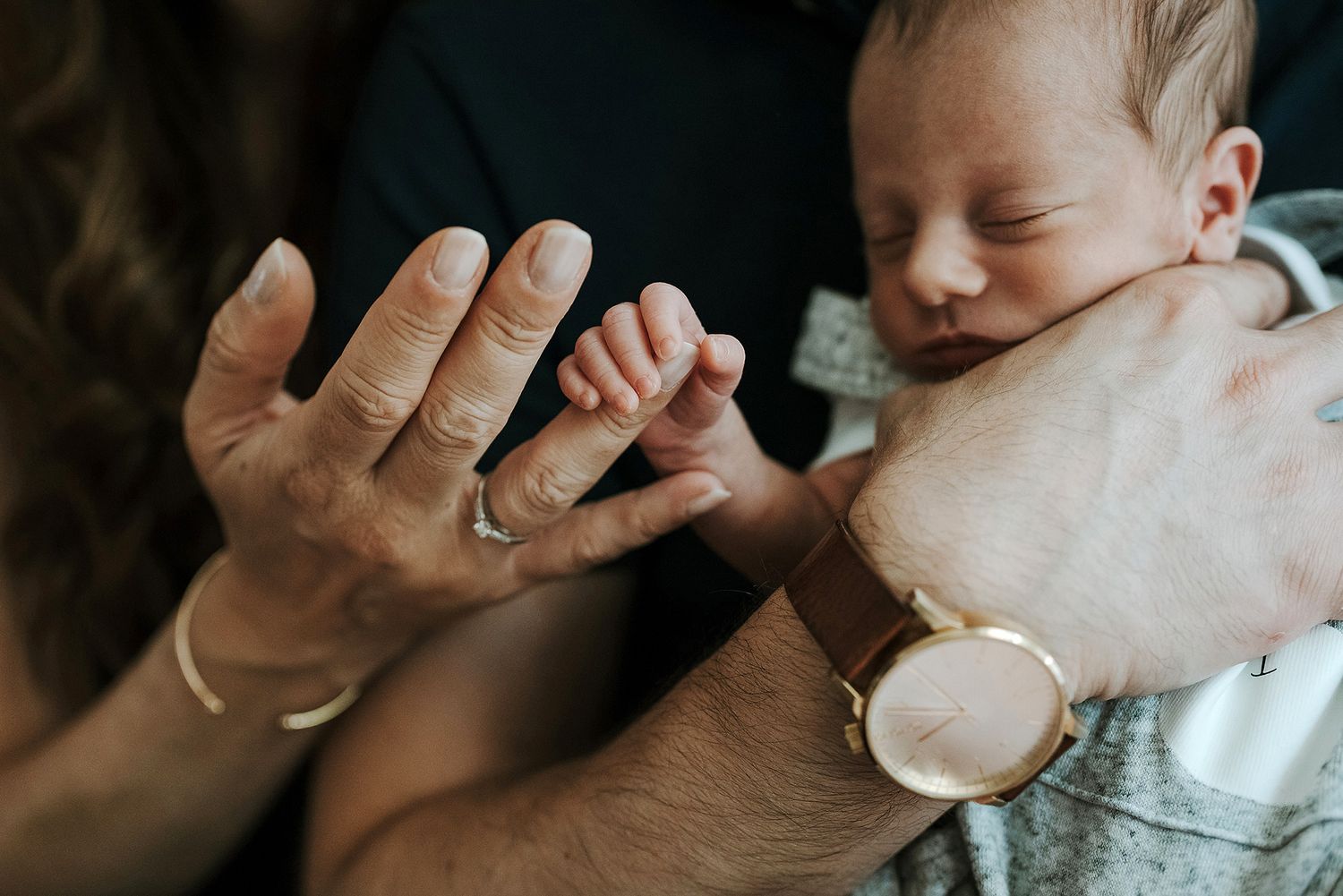 Close-up details of gentle hands holding a sleeping newborn.