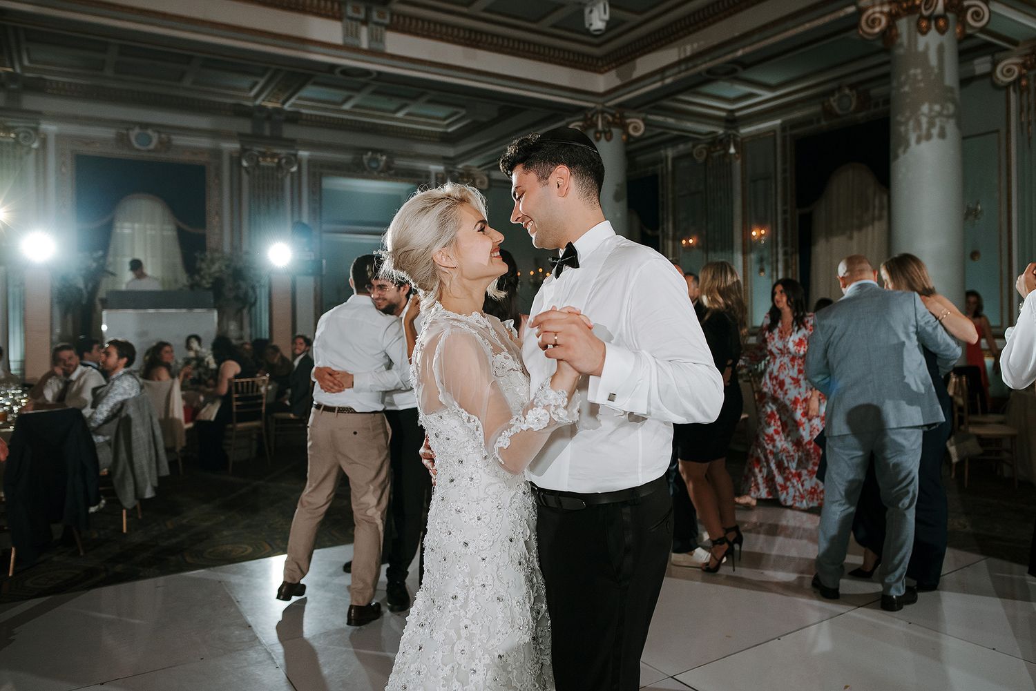 Wedding reception dance floor scene with guests celebrating in a dimly lit indoor venue.