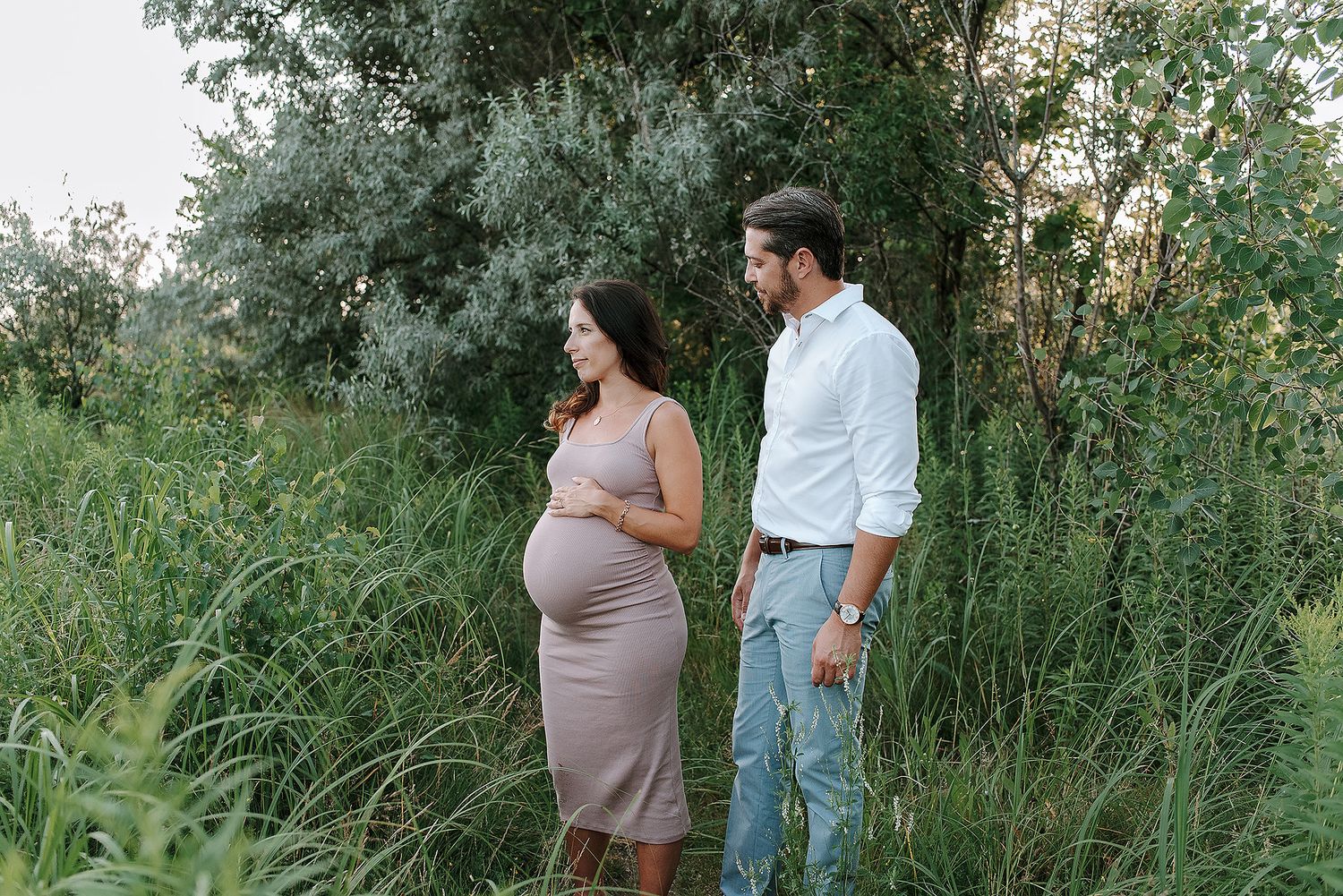 Expectant couple shares intimate moments in a natural outdoor setting.