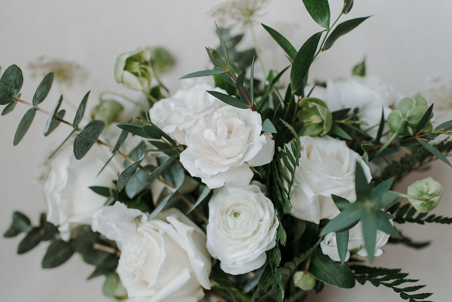 White roses and eucalyptus greenery create an elegant floral arrangement against a light neutral background.