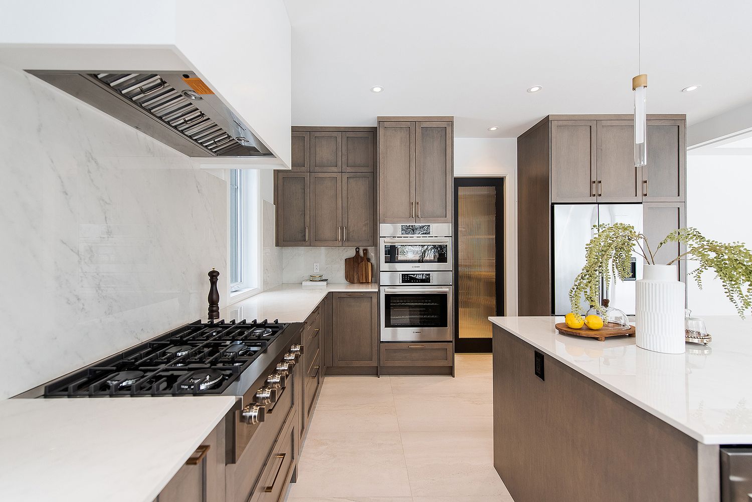 Modern kitchen features sleek brown cabinets, white countertops, and stainless steel appliances with marble backsplash.