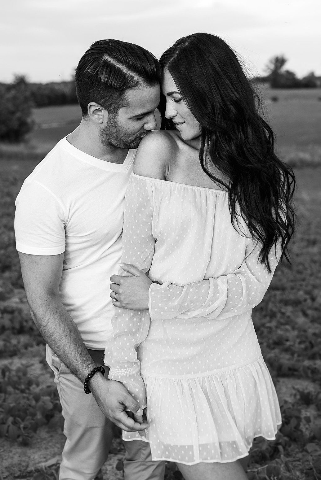 A romantic black and white photo series shows a couple embracing in a field wearing white outfits.