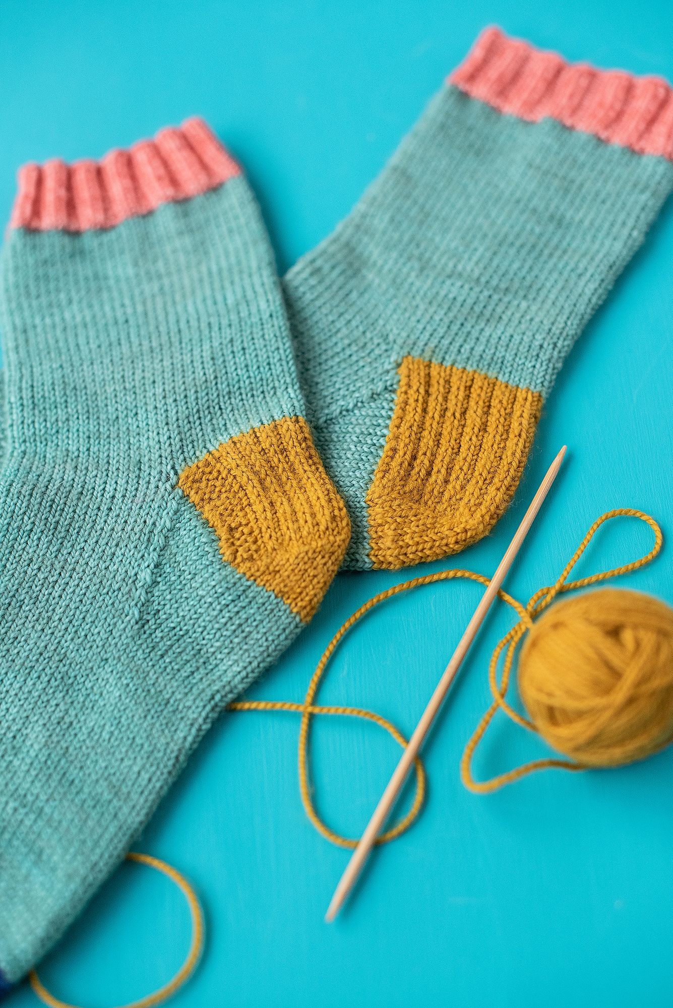 Mint green knitted sock with yellow toe being repaired with matching yarn.