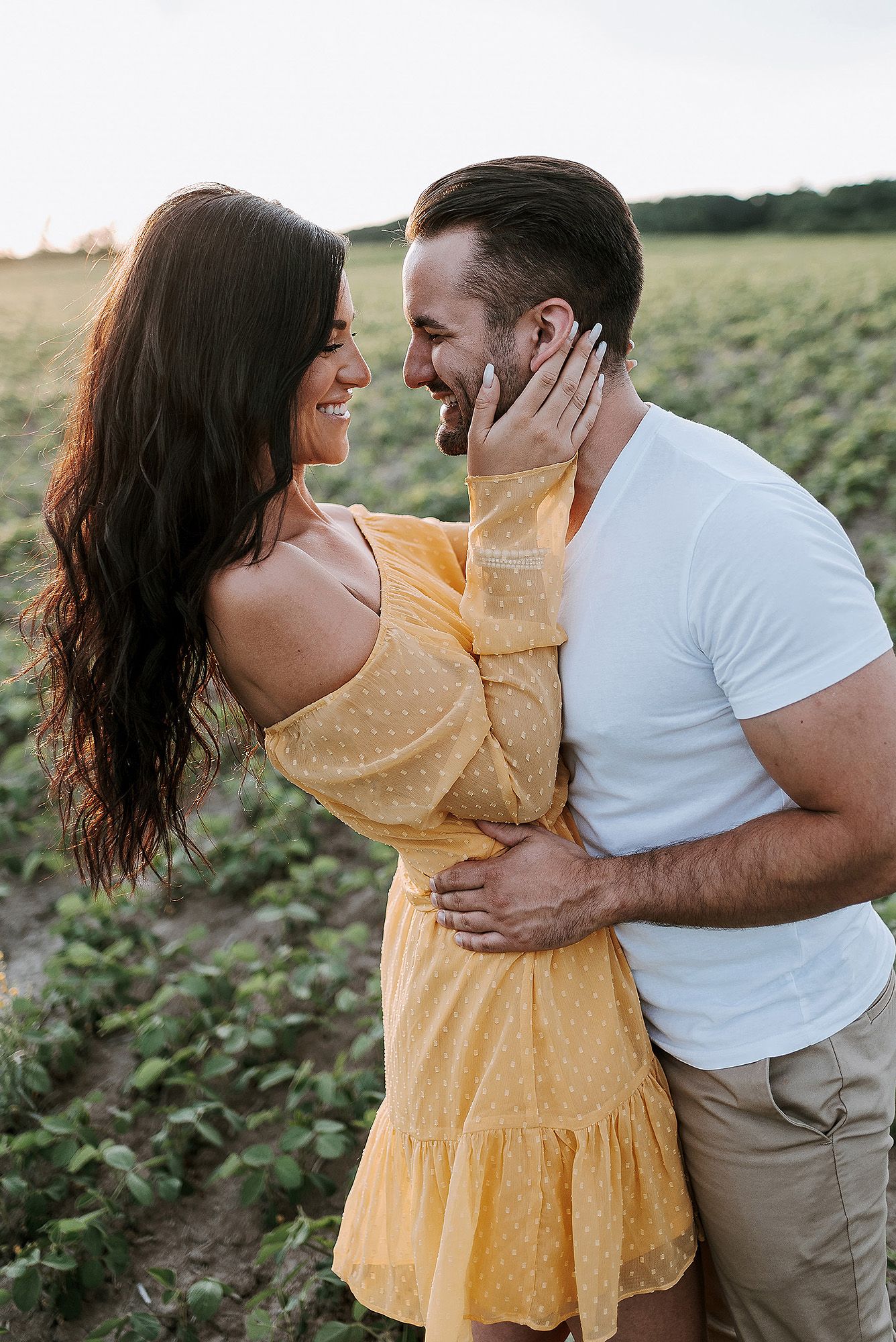 A couple in yellow dress and white shirt share intimate moments in a field during sunset.