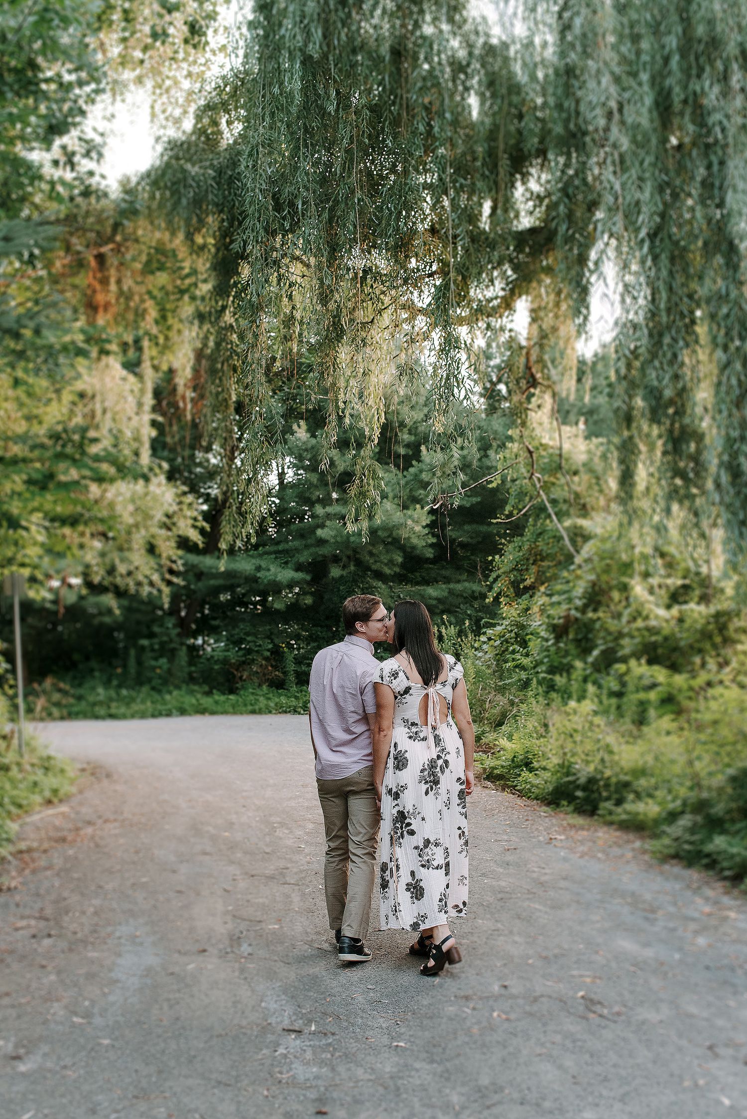 A couple walks along a scenic garden path under hanging moss and lush greenery on a peaceful afternoon.