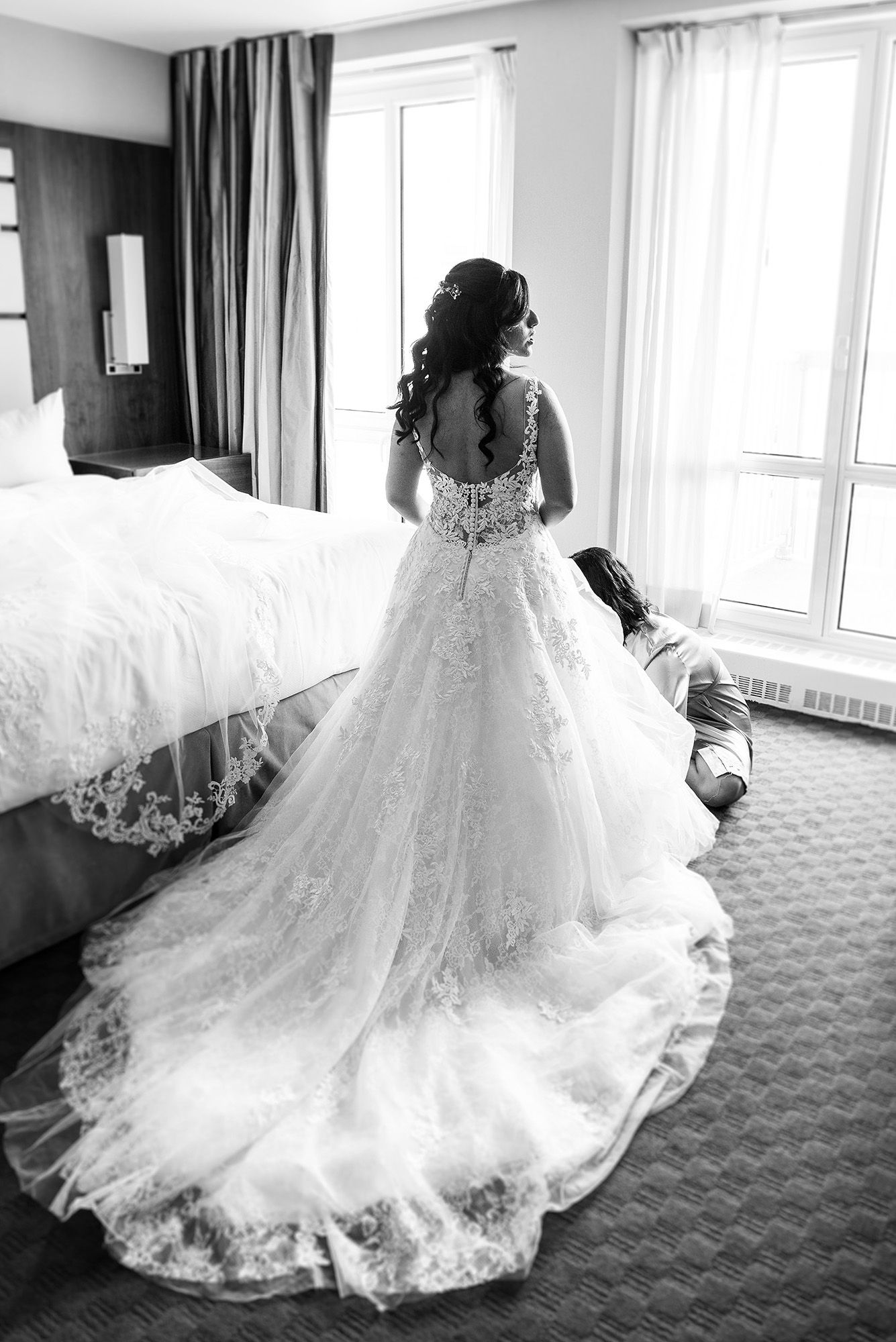Elegant white wedding dress with lace details and flowing train displayed in a sunlit hotel room.