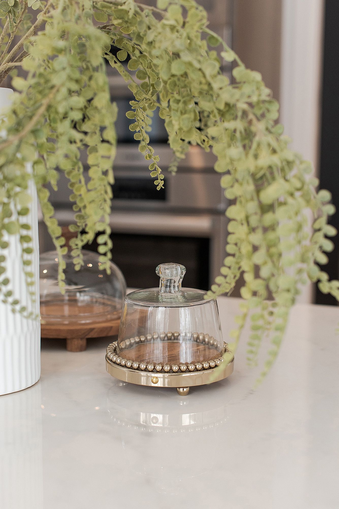 Glass candle holders with decorative beaded trim displayed beneath cascading green foliage.