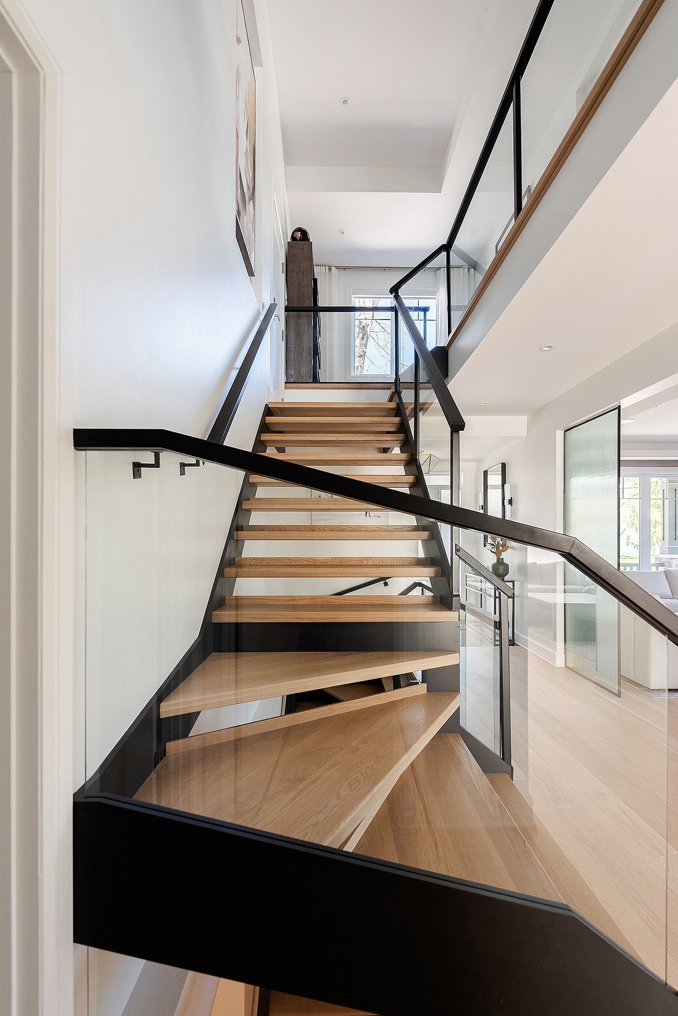 Modern floating staircase with wooden treads and black metal railings in a bright white interior space.