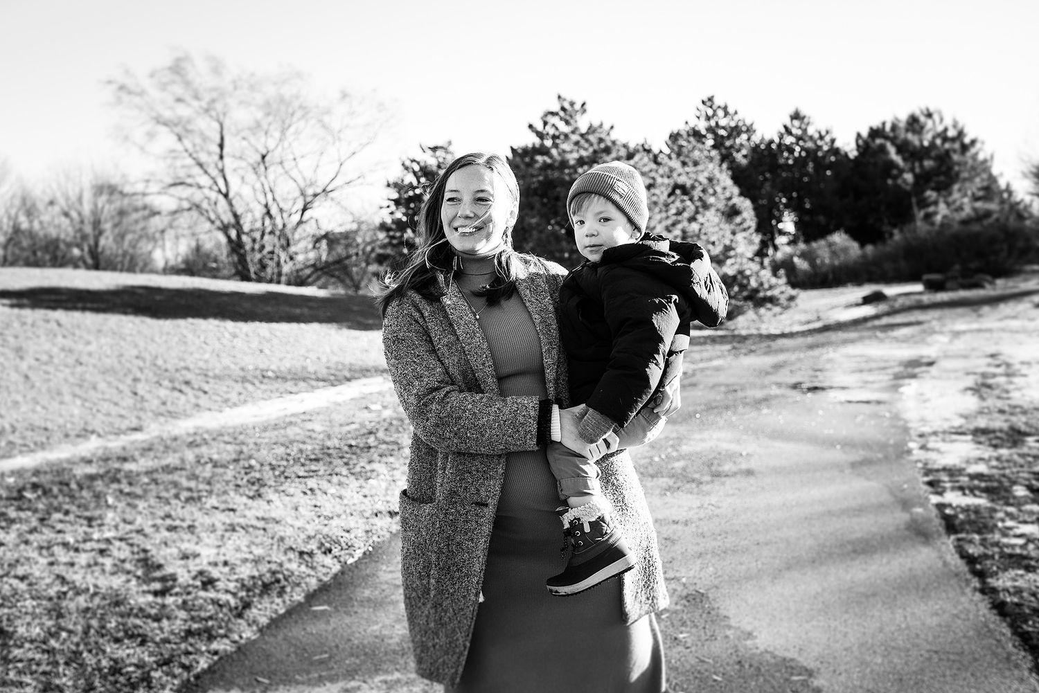 Outdoor maternity photo session on a winding path surrounded by trees.