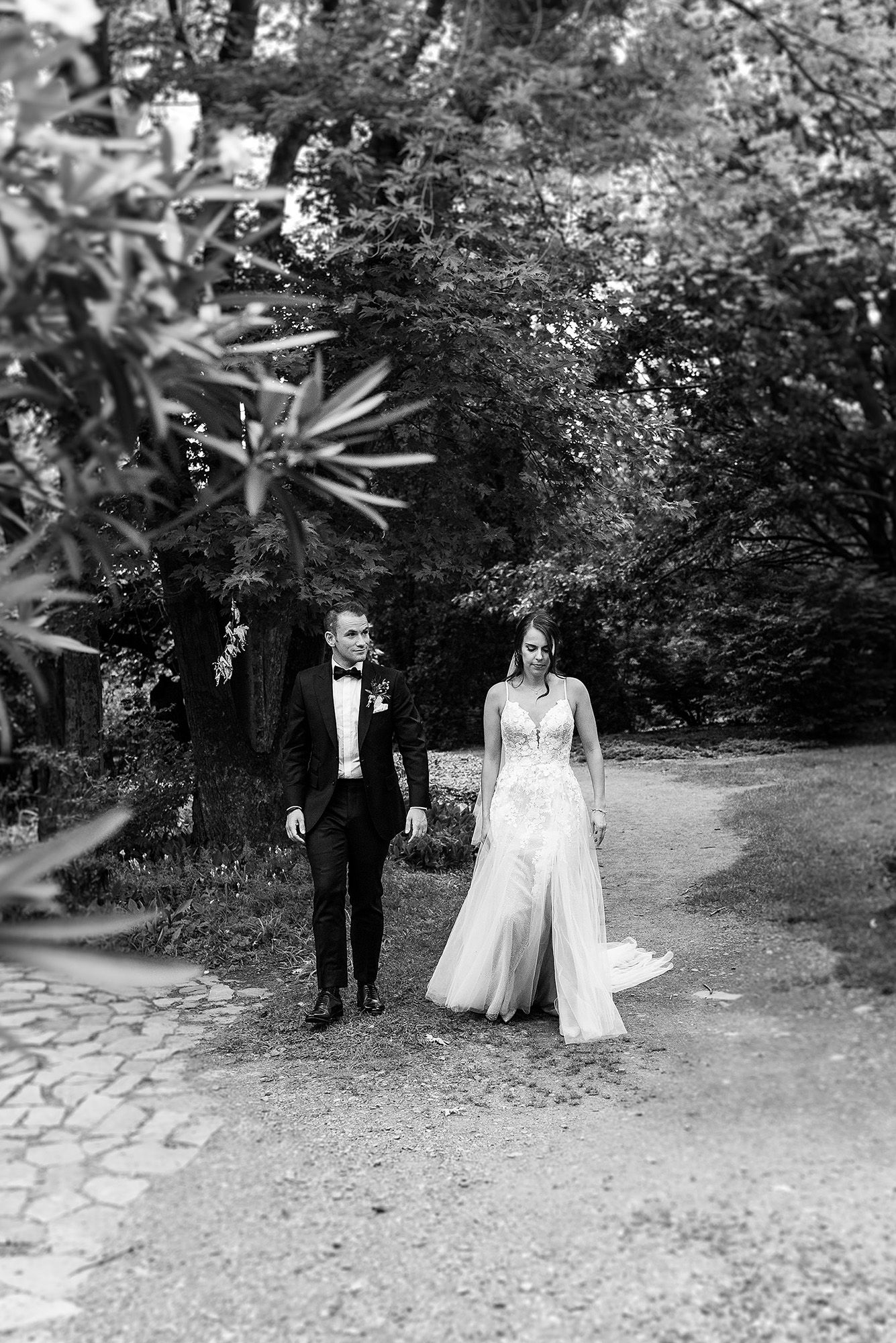 A romantic black and white photo series showing a couple in formal wedding attire walking together through a garden path.
