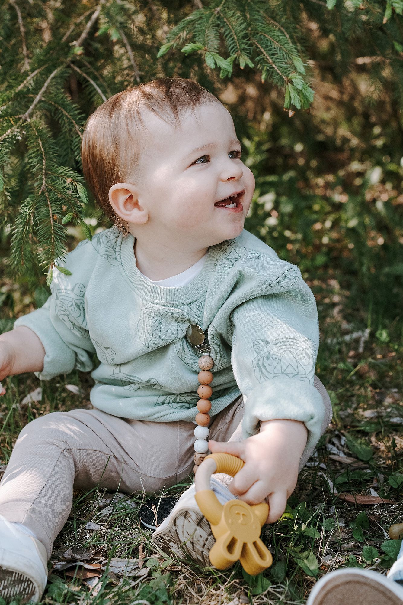Child in mint green jacket playing with wooden toys on forest floor.