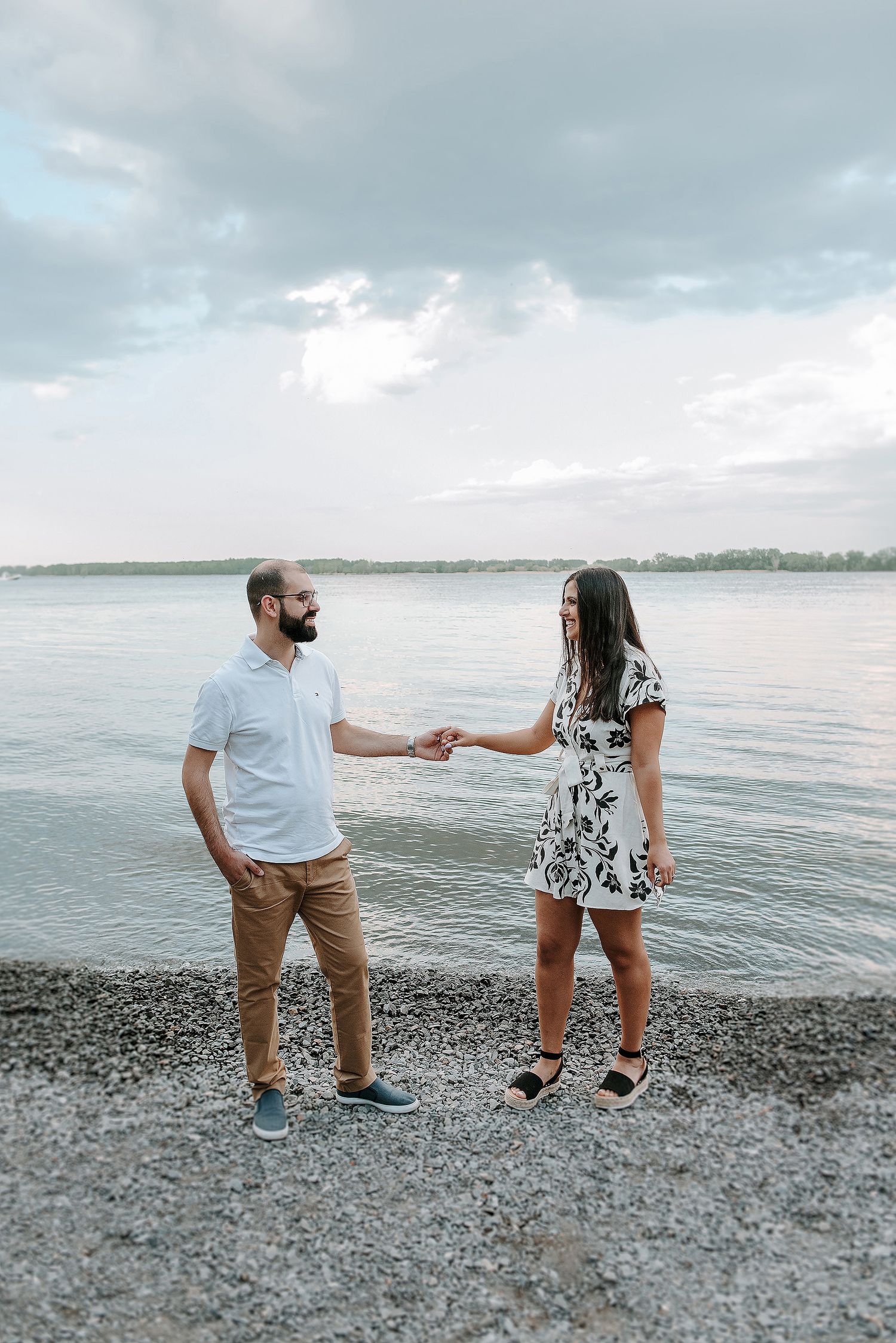A couple stands on a rocky beach at sunset, playfully interacting with each other near the water's edge.